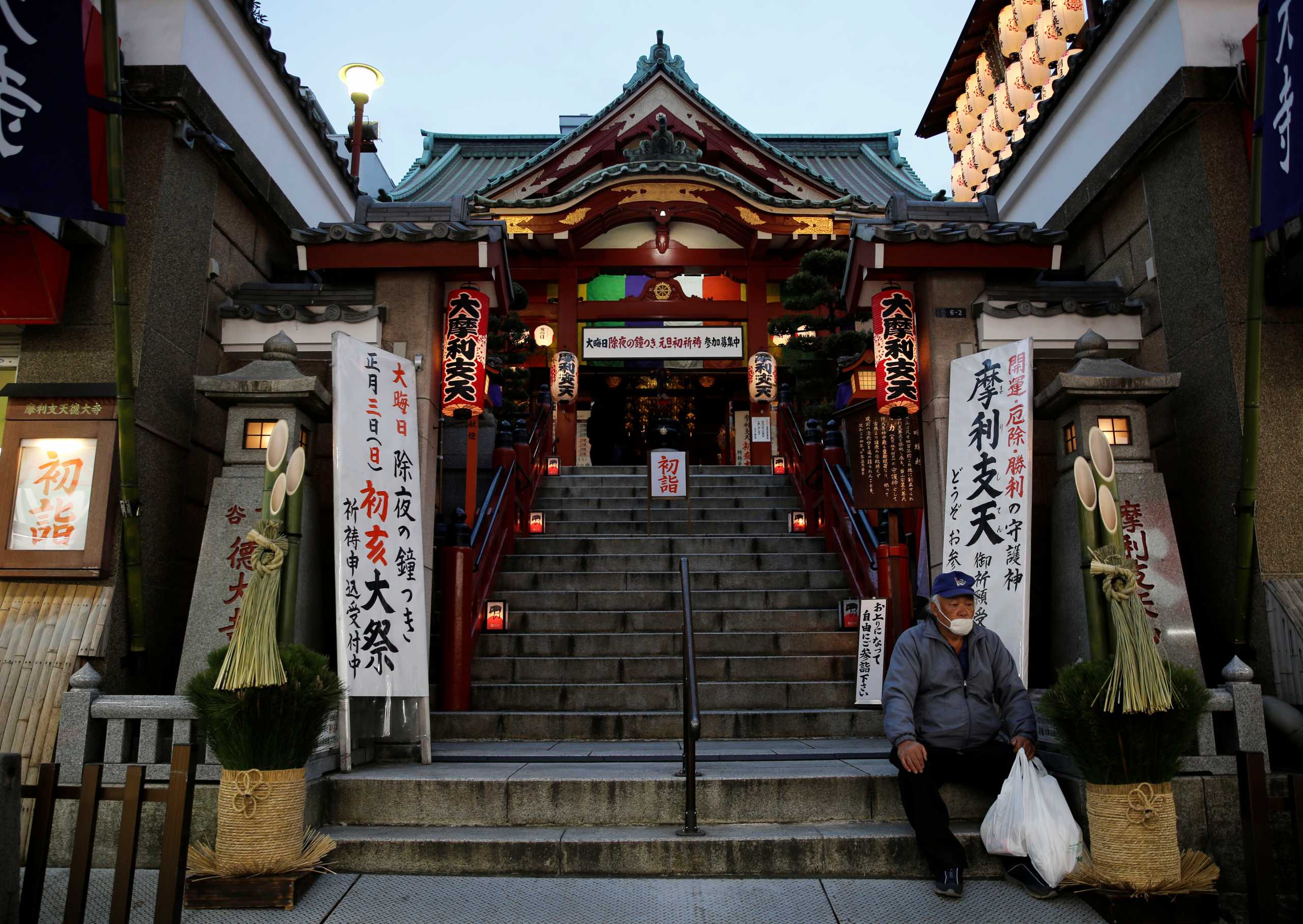 A man sits next to a new year's decoration in front of a temple in Tokyo, Japan, December 29, 2020. REUTERS