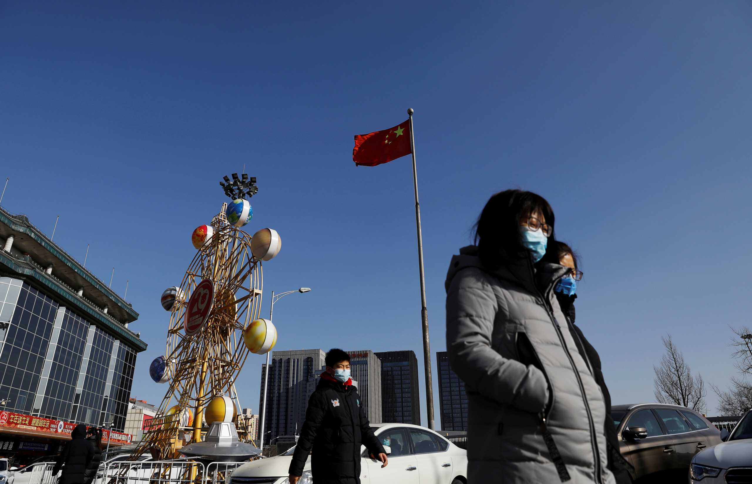 People wearing face masks walk past a Chinese flag, following new cases of the coronavirus disease (COVID-19) in the country, in Beijing, China January 11, 2021. REUTERS