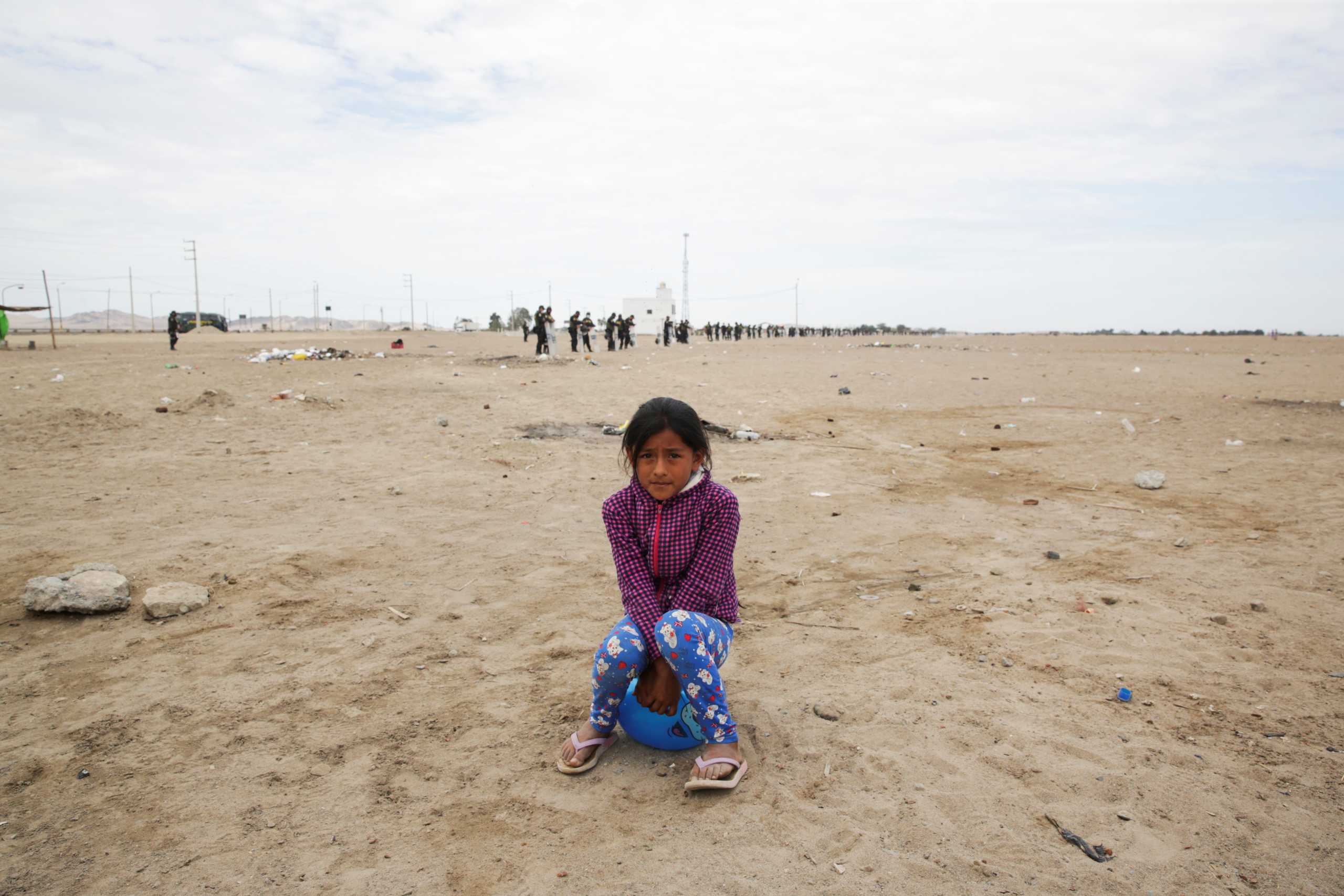 A little girl sits on a ball as police stand guard to prevent protests from workers from agricultural export companies over an agreement to reform the sector and address their complaints over poor pay, in Villacuri, Peru December 29, 2020. REUTERS
