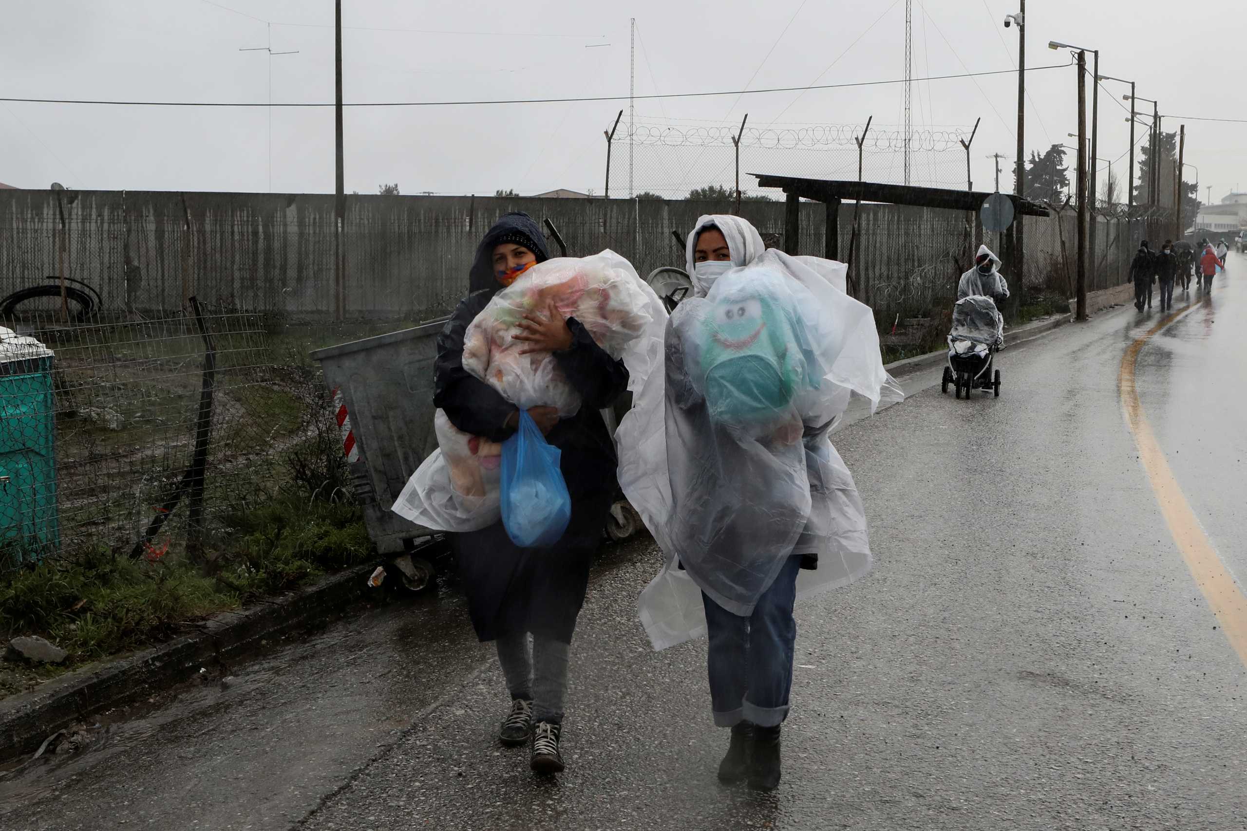 Two women carry their children during a rainfall, outside the Kara Tepe camp for refugees and migrants on the island of Lesbos, Greece, January 28, 2021. REUTERS