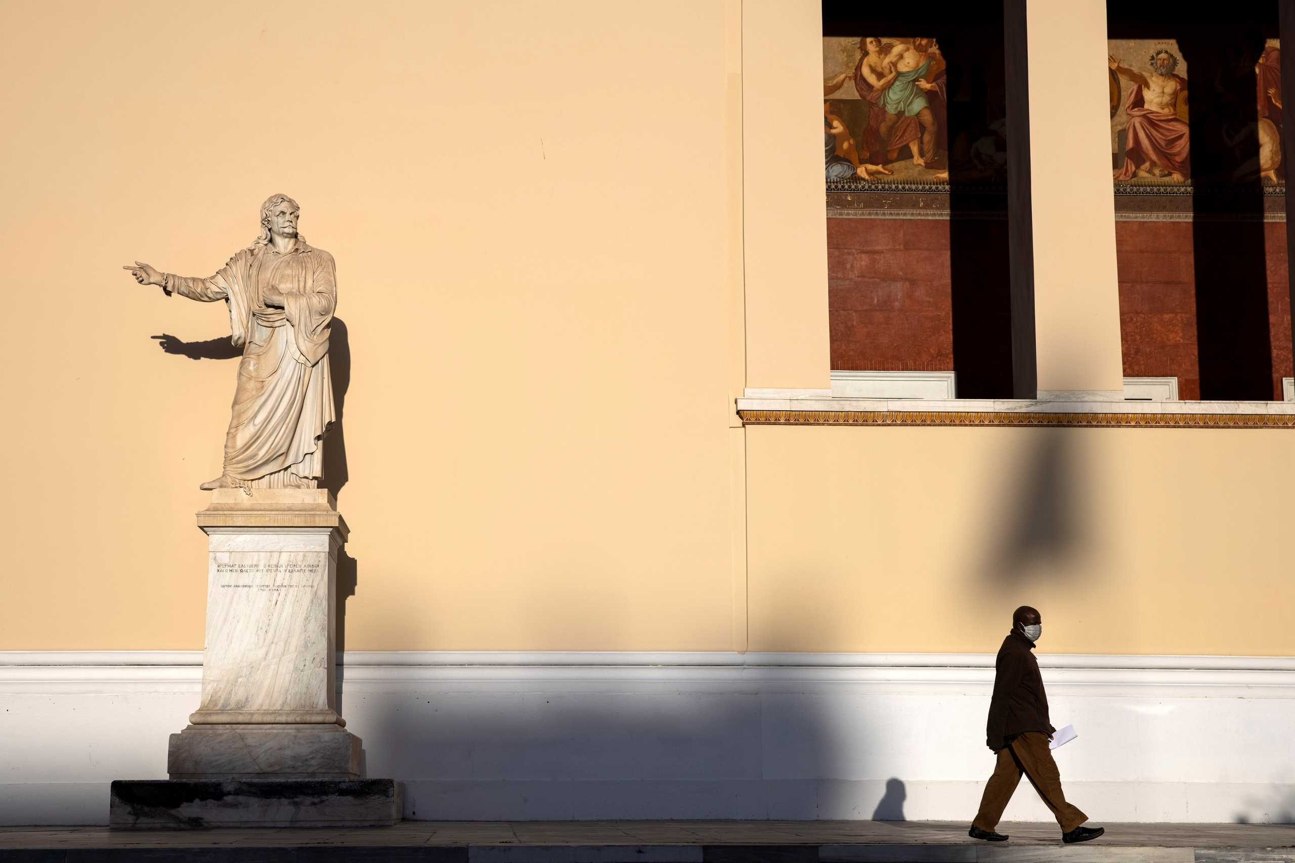 A man wearing a protective face mask walks past a statue of Rigas Feraios at the University of Athens, amid the coronavirus disease (COVID-19) pandemic, Greece, February 2, 2021. REUTERS