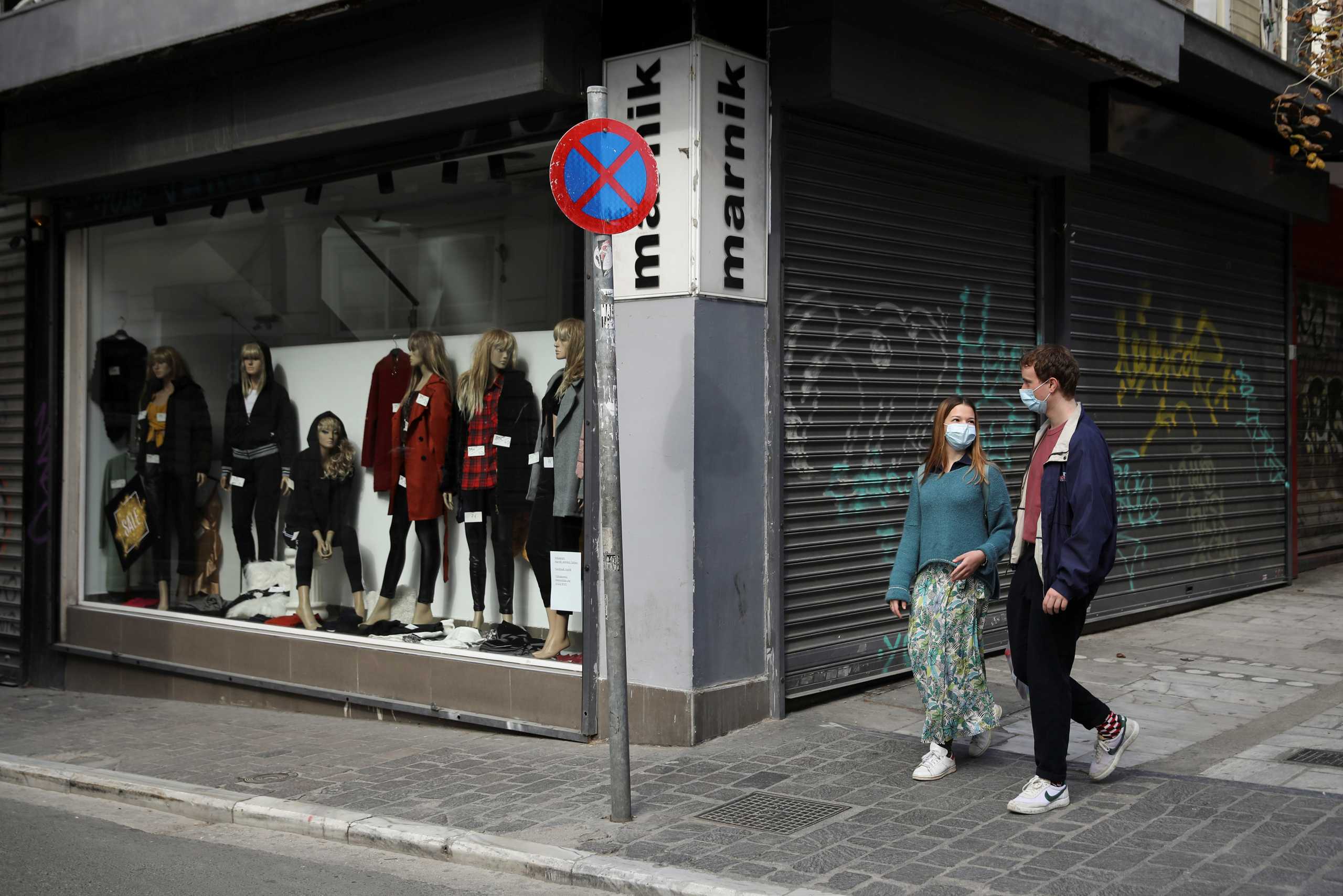 People wearing protective face masks walk past a closed shop, amid lockdown restrictions due to the spread of the coronavirus disease (COVID-19) pandemic, in Athens, Greece, February 6, 2021. REUTERS