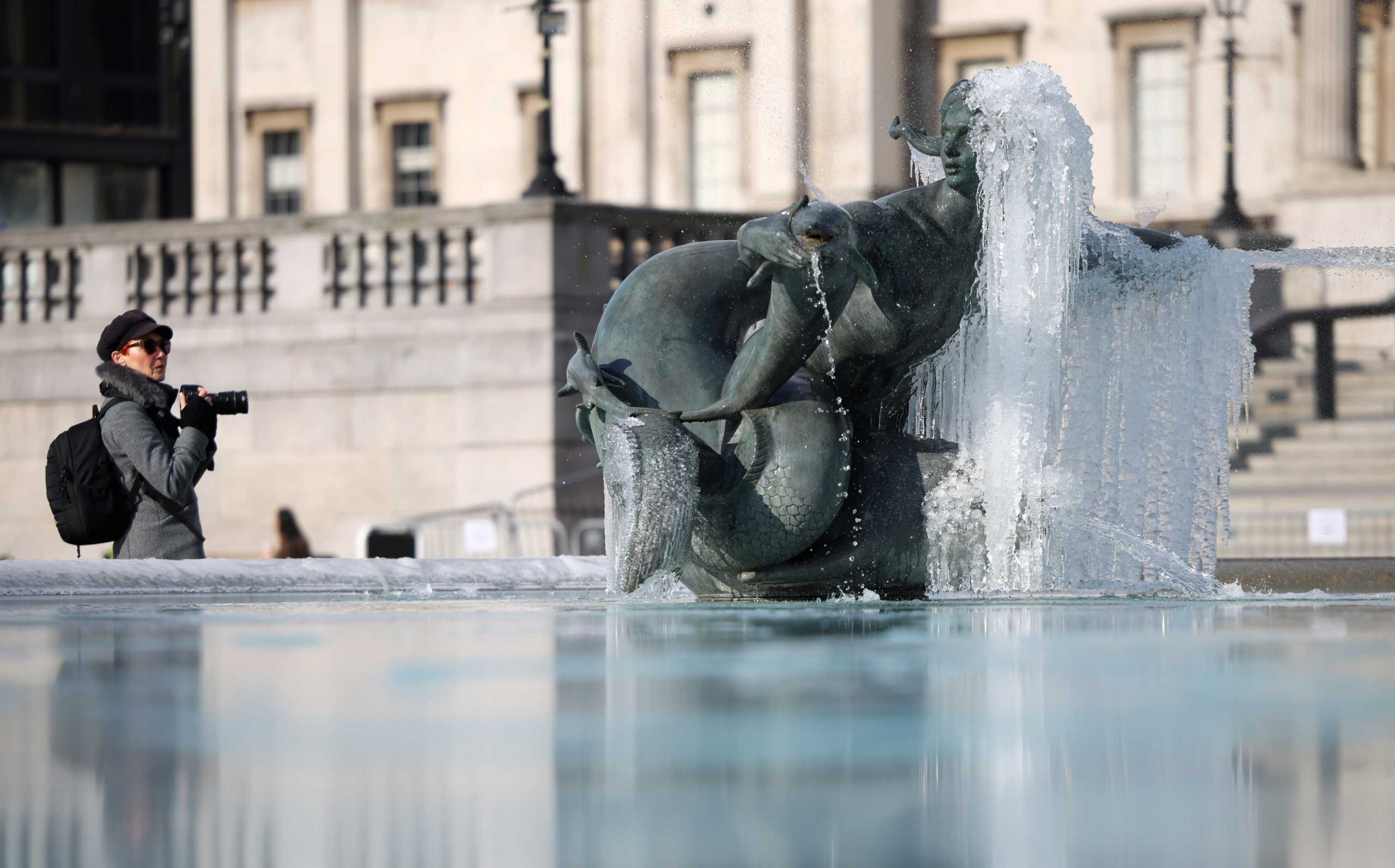 A photographer looks at a fountain covered in icicles in Trafalgar Square, London, Britain February 11, 2021. REUTERS