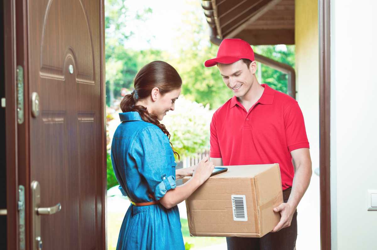 Delivery man standing at the door of the house and carrying parcels for young woman. Woman signing.