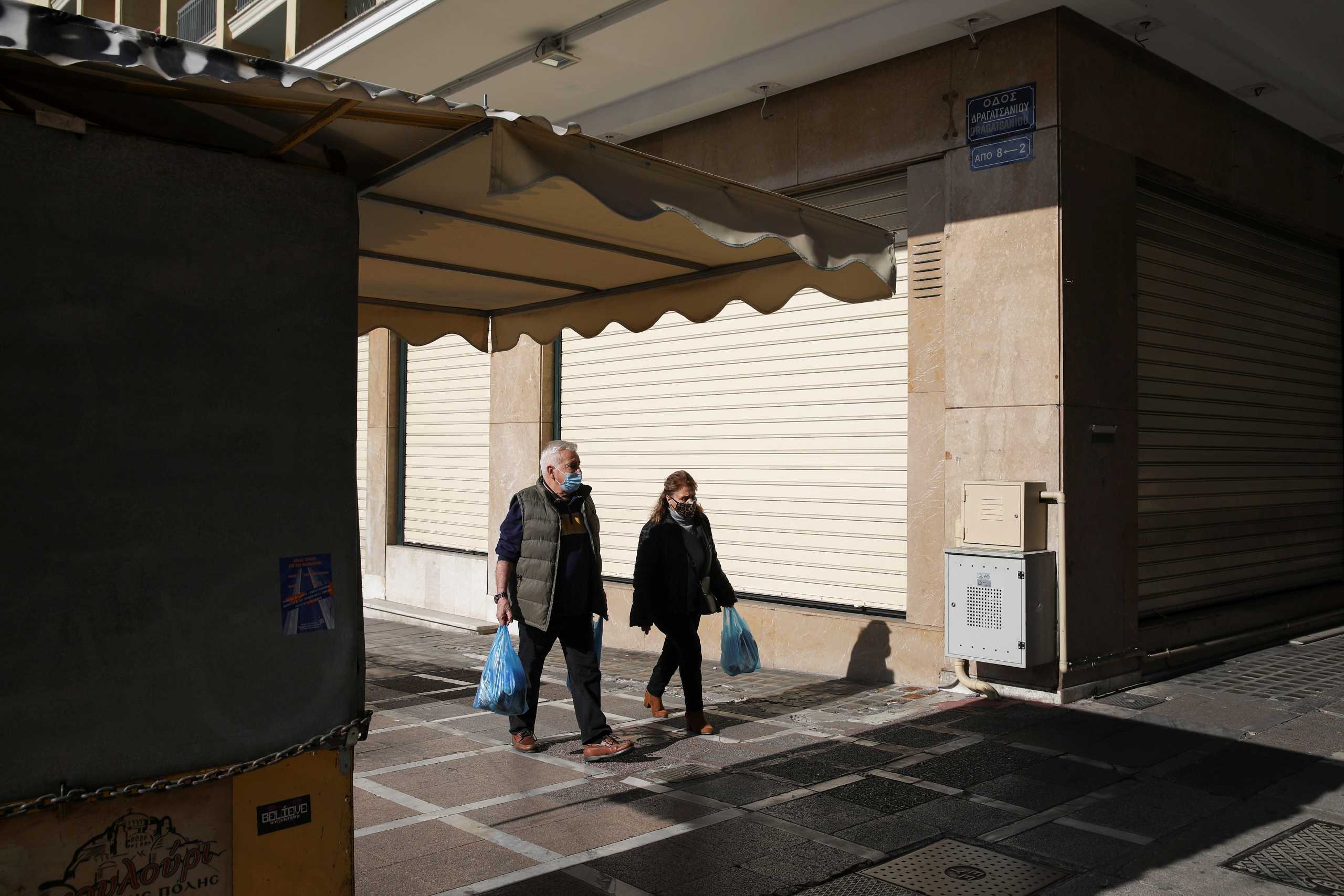 People wearing protective face masks walk past a closed shop, amid lockdown restrictions due to the spread of the coronavirus disease (COVID-19) pandemic, in Athens, Greece, February 6, 2021. REUTERS