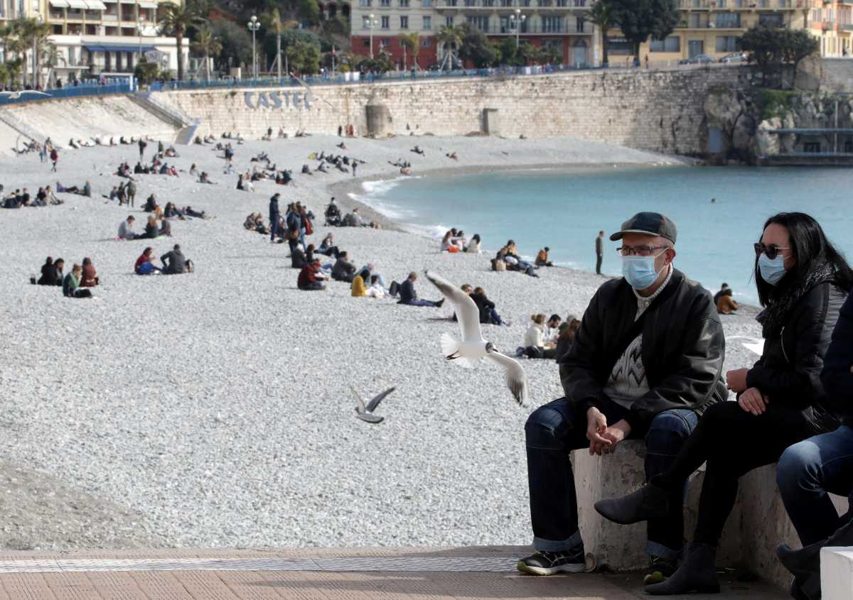 FILE PHOTO: People, wearing protective face masks, sit on the beach of the Promenade des Anglais in Nice amid the coronavirus disease (COVID-19) outbreak in France, February 18, 2021.    REUTERS