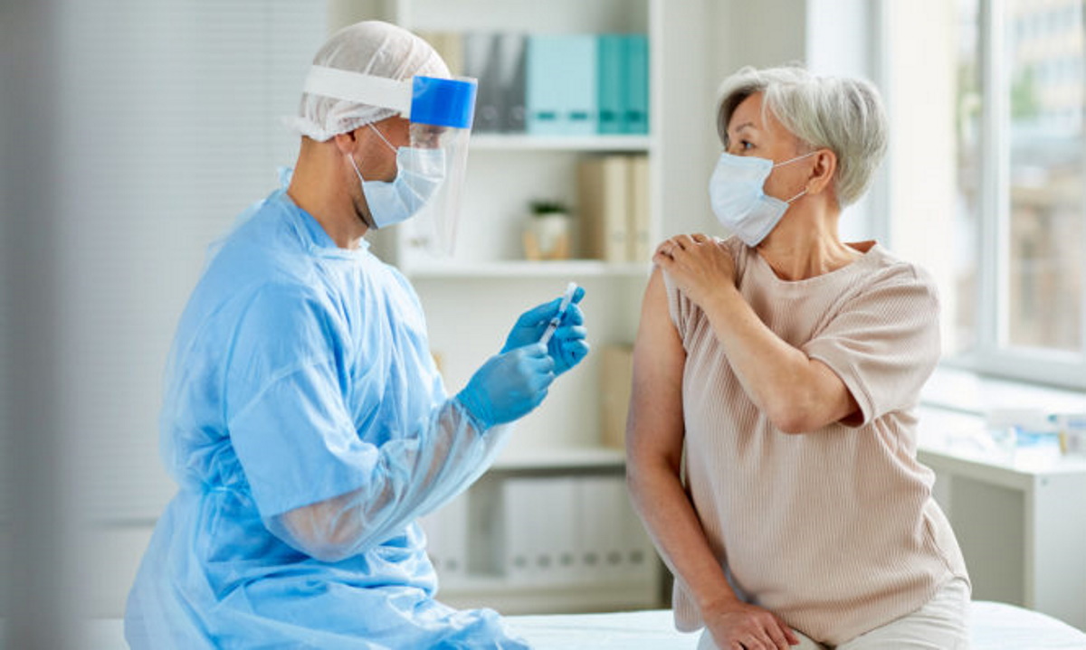 Side view shot of male nurse wearing protective mask and gloves preparing medical syringe for giving injection to senior patient (Side view shot of male nurse wearing protective mask and gloves preparing medical syringe for giving injection to senior