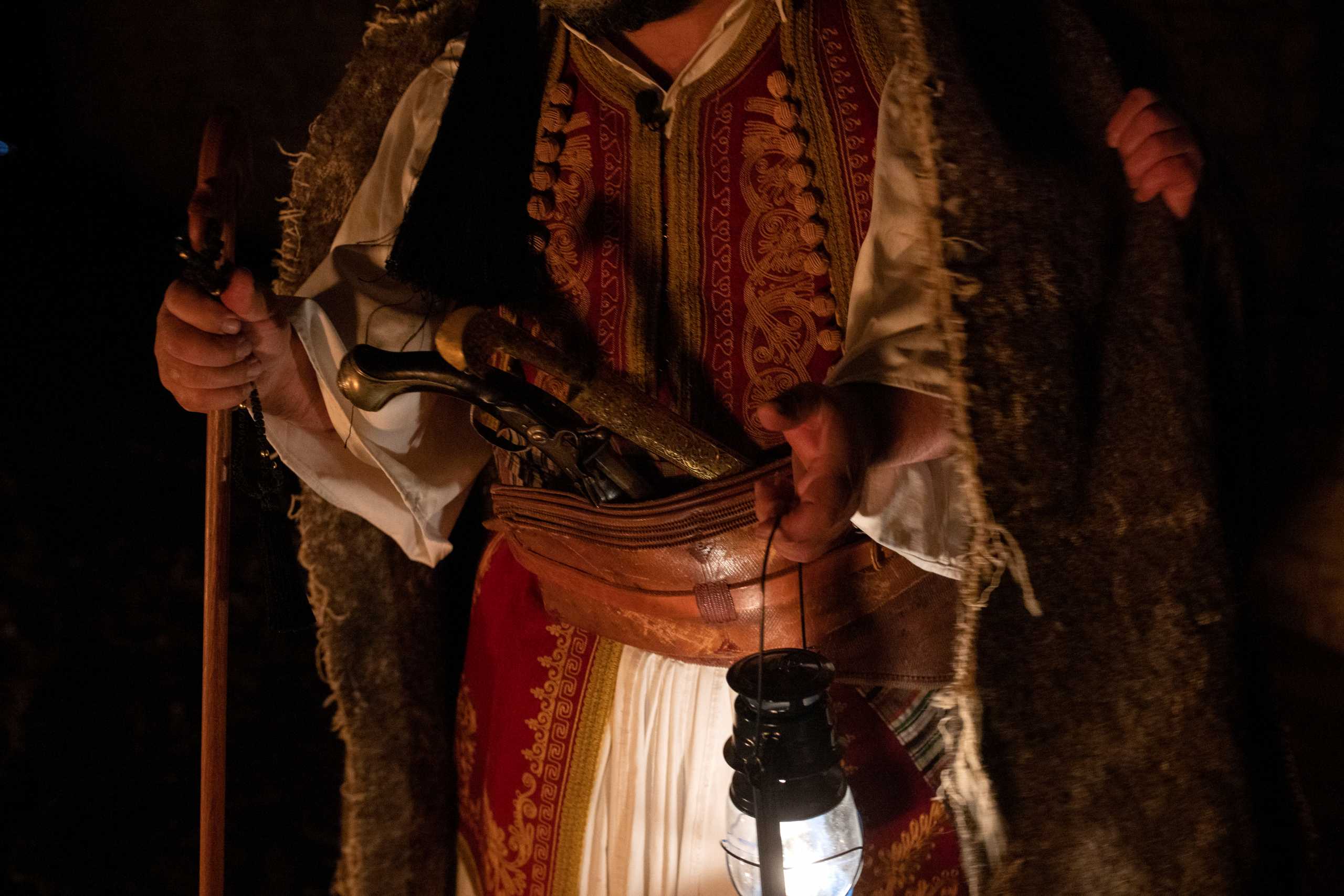 A member of a local theatre group dressed in a traditional costume carries historical weapons and a lantern as he takes part in re-enacting a popular account of the beginning of the 19th century Greek War of Independence at the monastery of Agia Lavra, in the town of Kalavrita, Greece, March 16, 2021. Picture taken March 16, 2021. REUTERS