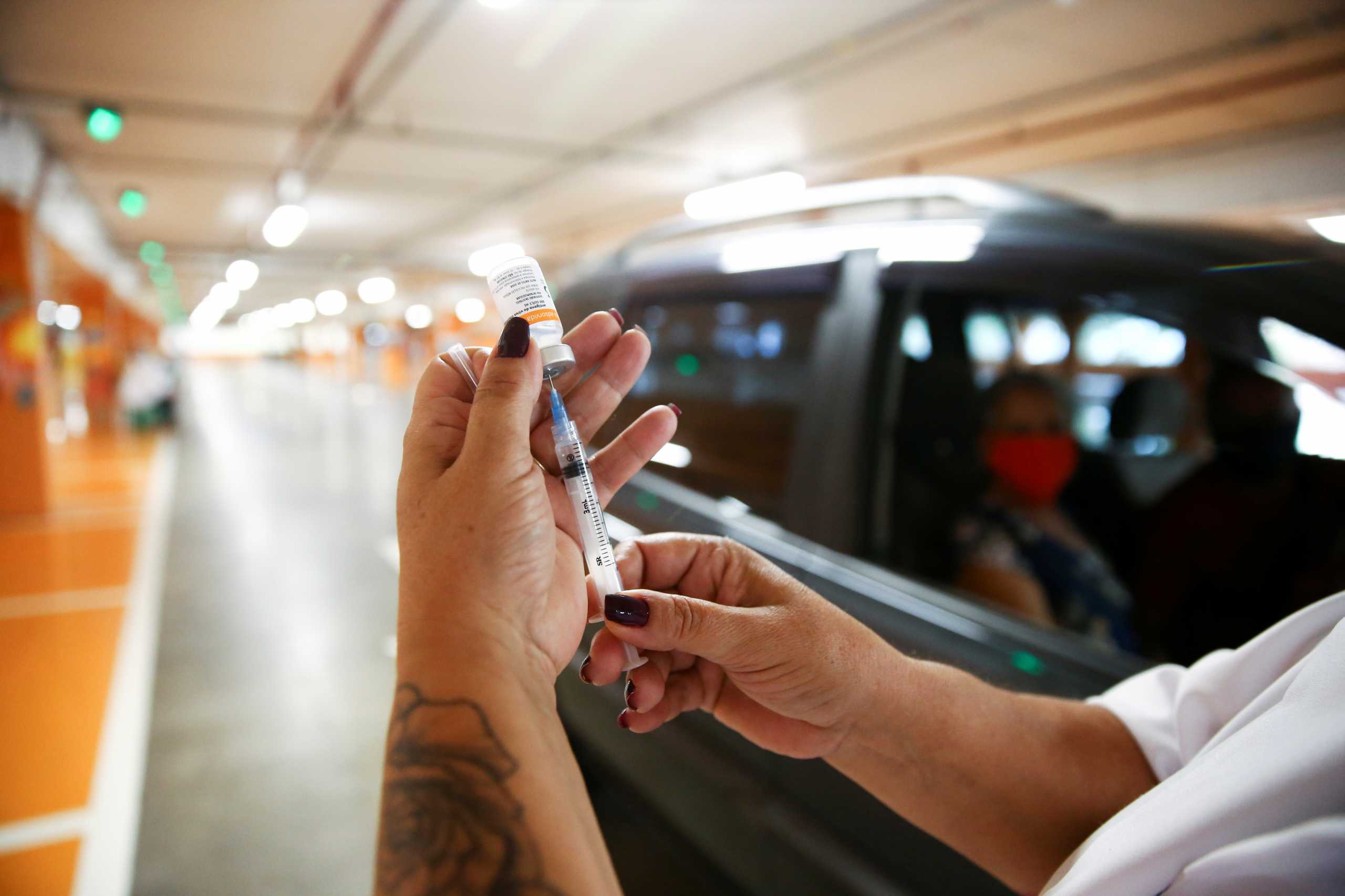 A health worker prepares to vaccinate a senior citizen with a dose of the Sinovac's coronavirus disease (COVID-19) vaccine at a drive-thru vaccination spot in the garage of a supermarket in Porto Alegre, Brazil March 18, 2021. REUTERS