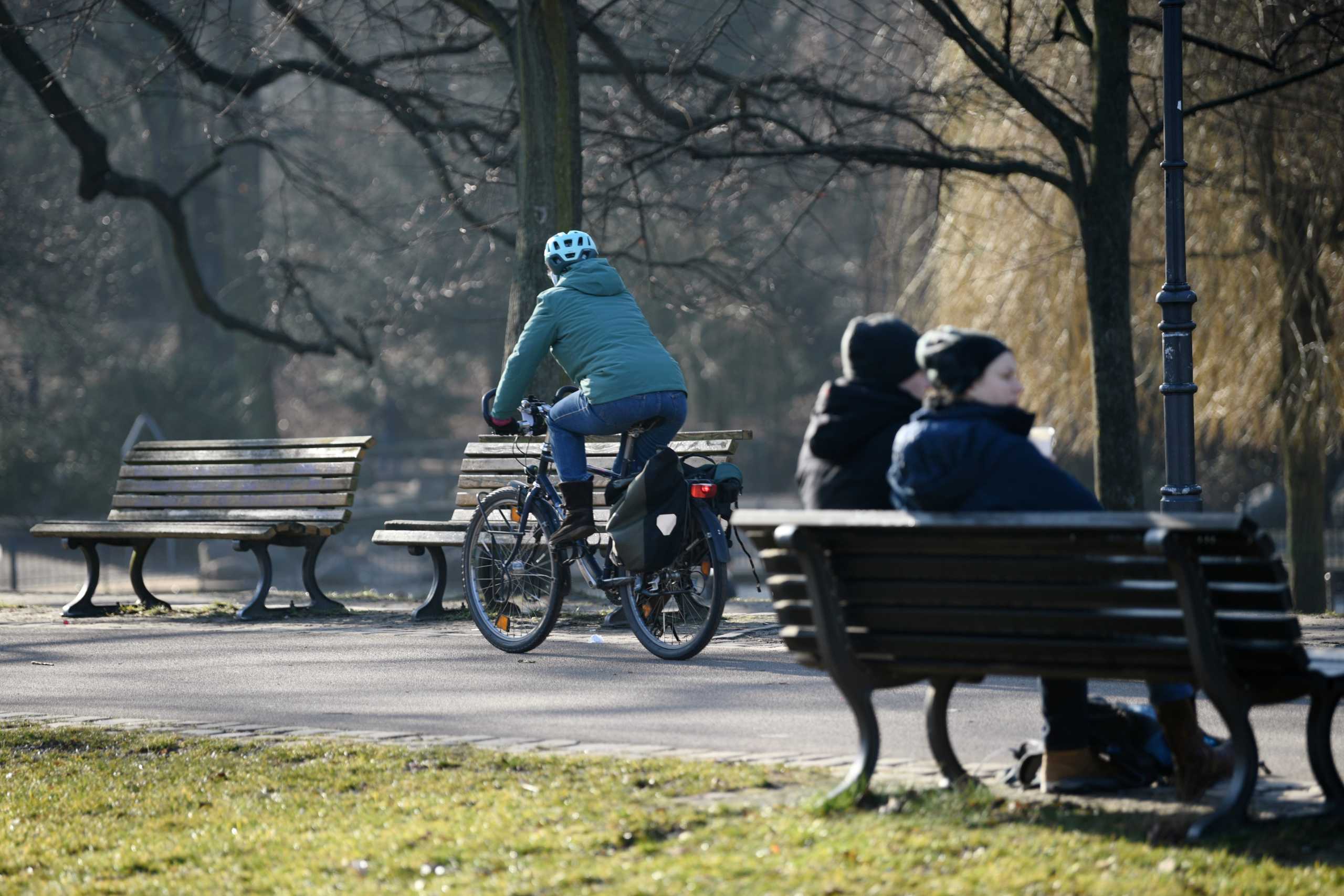 A cyclist drives past people sitting on a park bench at the Volkspark Friedrichshain, amid the coronavirus disease (COVID-19) pandemic, in Berlin, Germany March 2, 2021.  REUTERS