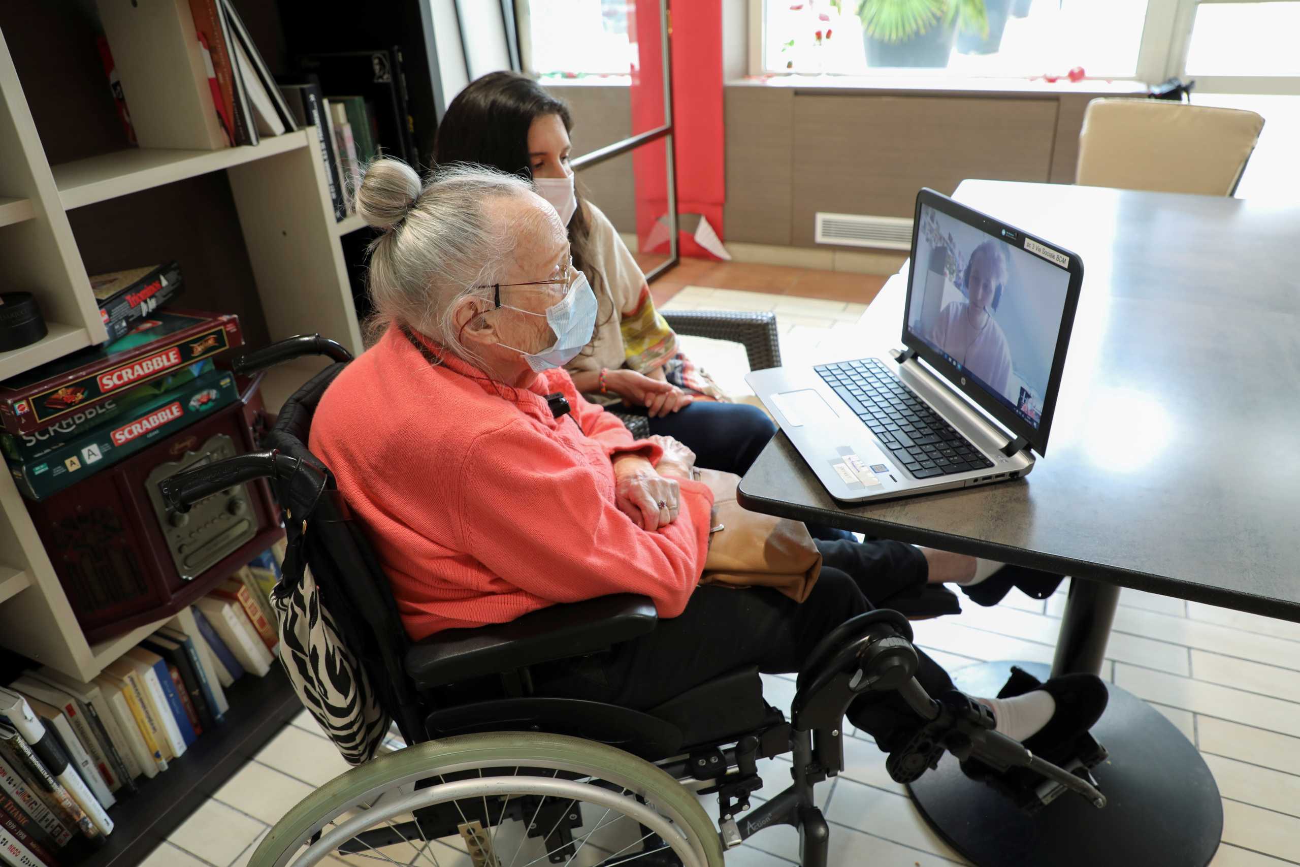 Elderly care home resident Jacqueline Tolu, 98, sits beside carer Christal Perthuis as they attend a video conference with English student Elliot Bellman, 20, using ShareAmi scheme that links students studying French with elderly people to beat lockdown blues, in Bonneuil-sur-Marne, France, March 22, 2021. Picture taken March 22, 2021.   REUTERS