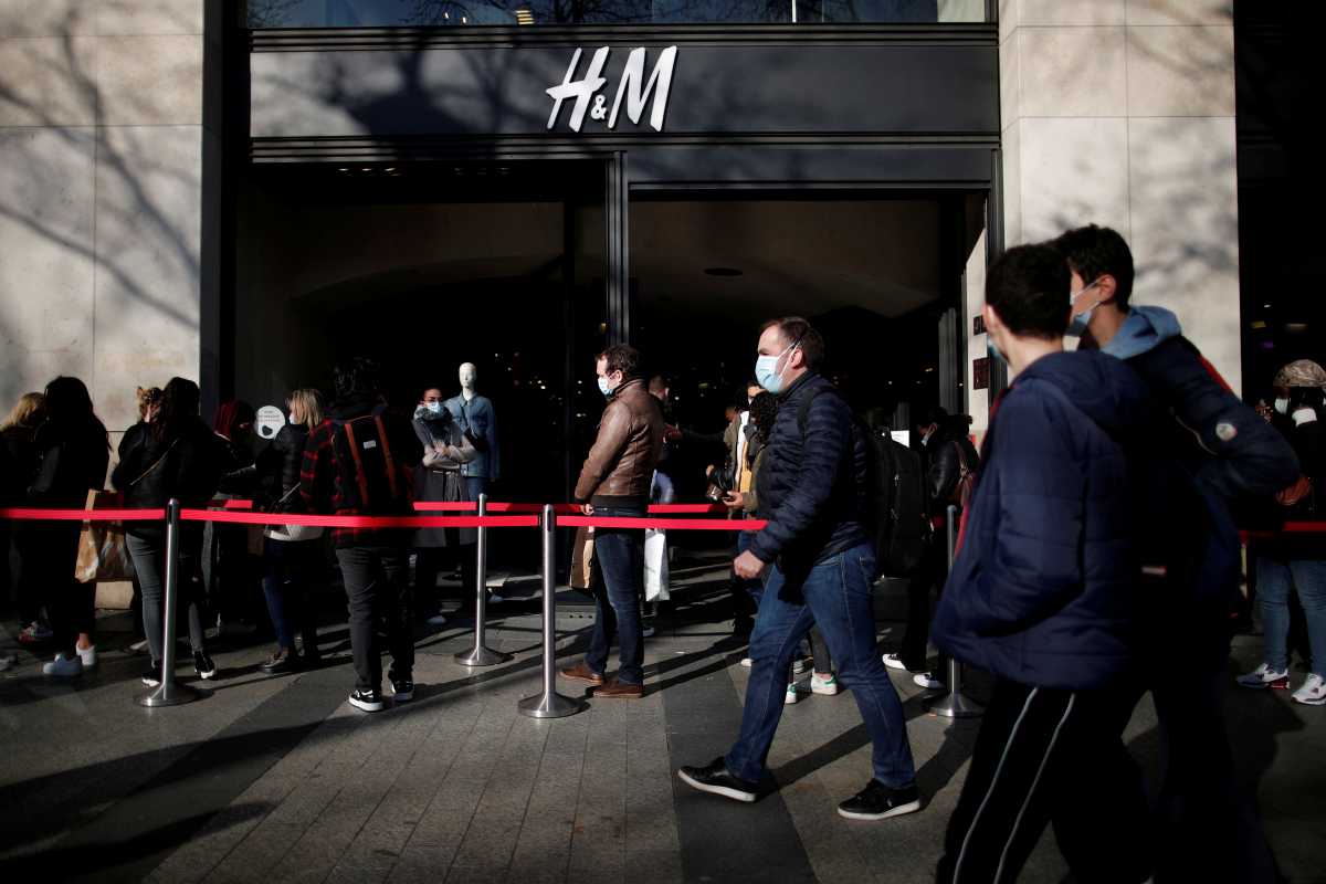 FILE PHOTO: People, wearing protective face masks, queue outside an H&M clothing store on the Champs Elysees avenue in Paris, France, March 19, 2021. REUTERS