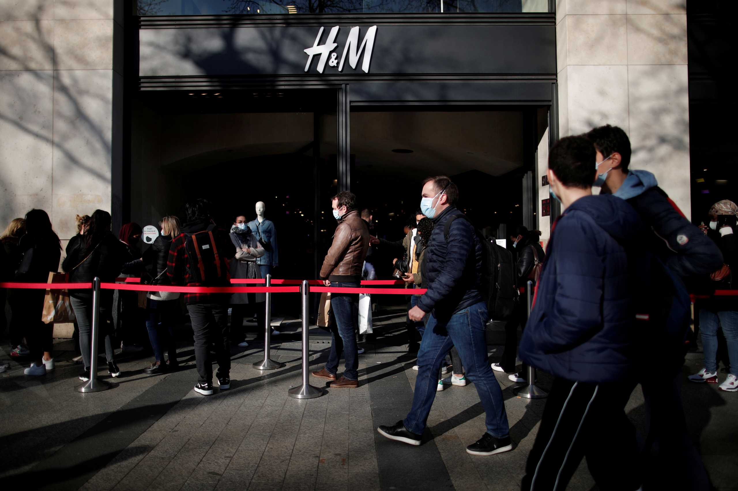 FILE PHOTO: People, wearing protective face masks, queue outside an H&M clothing store on the Champs Elysees avenue in Paris, France, March 19, 2021. REUTERS