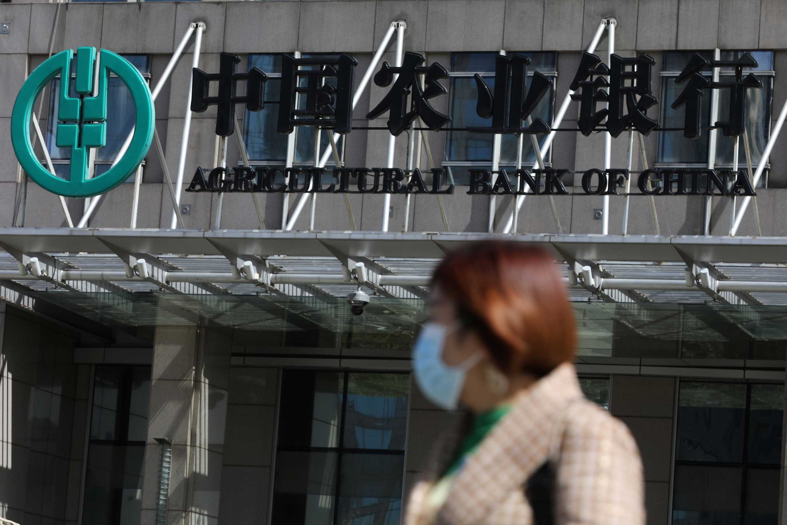 A woman walks past an office building of Agricultural Bank of China, in Beijing, China March 29, 2021. REUTERS