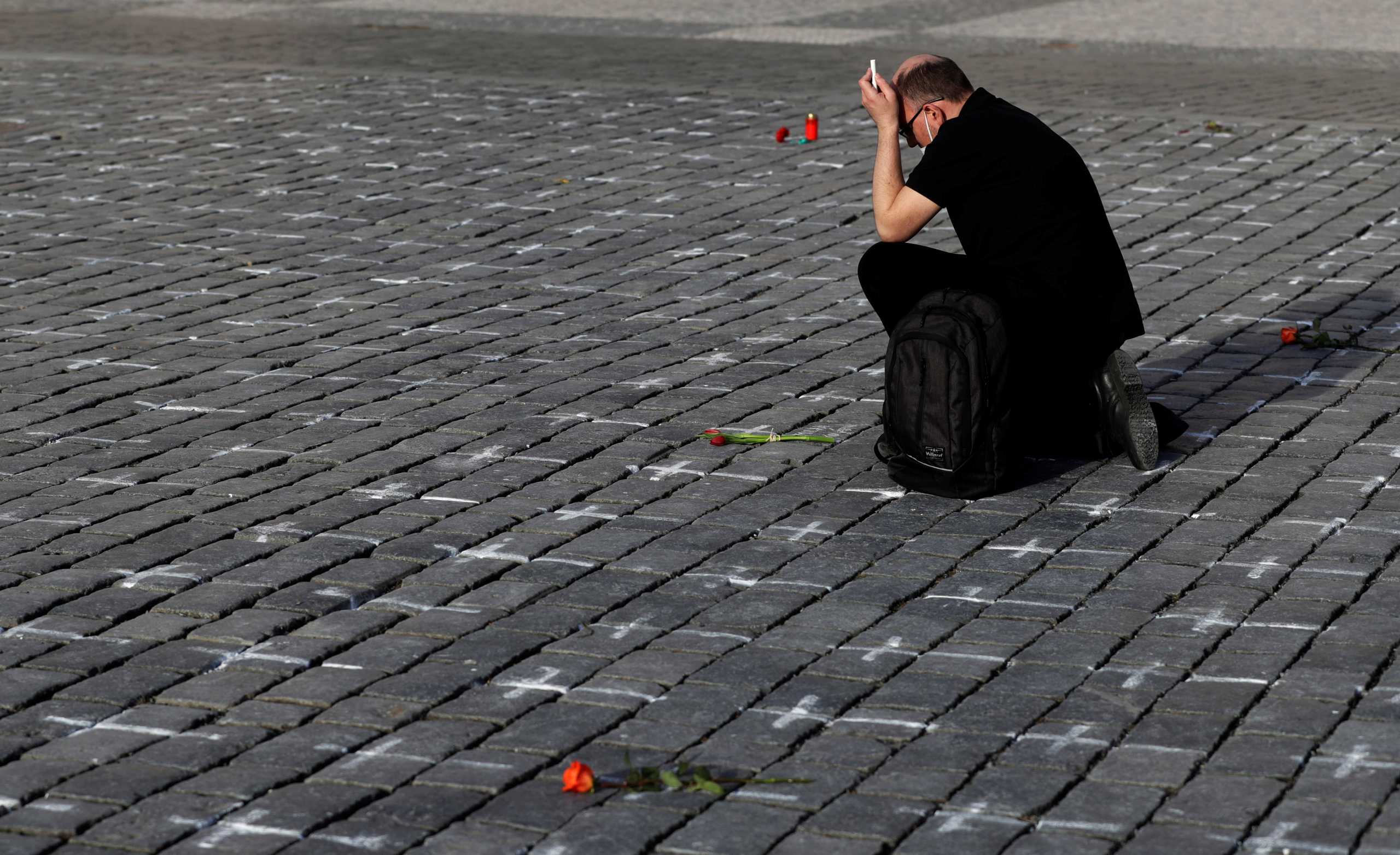 A man mourns for his deceased loved one at the Old Town Square where thousands of crosses have been painted on a pavement to commemorate the first anniversary since the death of the first Czech coronavirus disease (COVID-19) patient in Prague, Czech Republic, March 25, 2021. Picture taken March 25, 2021. REUTERS