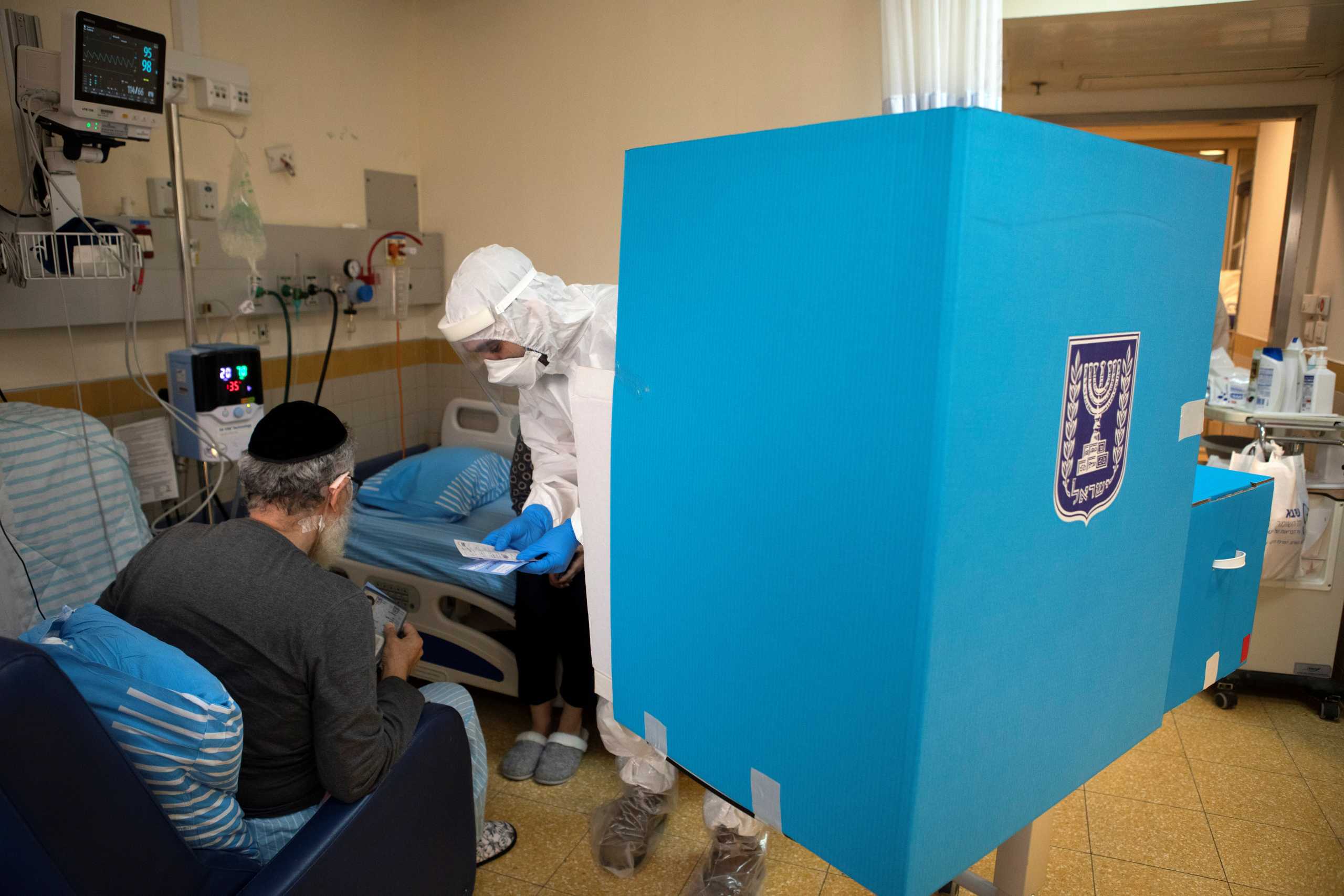 A hospital employee wearing personal protective equipment (PPE), assists a patient in a ward for the treatment of the coronavirus disease (COVID-19), before he casts his ballot in a mobile ballot box as Israelis vote in a general election, at Sheba Medical Center in Ramat Gan, Israel March 23, 2021. REUTERS