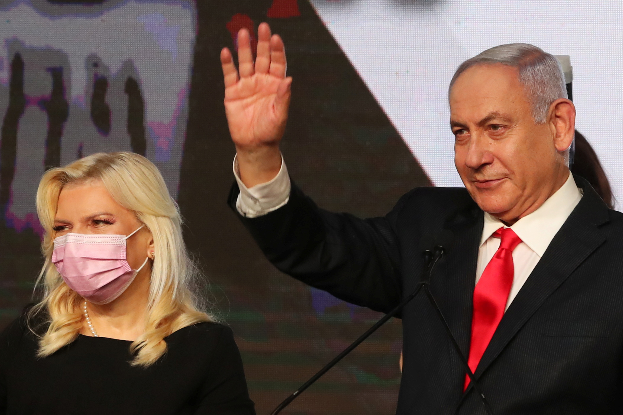 Israeli Prime Minister Benjamin Netanyahu stands next to his wife Sara as he waves while delivering a speech to supporters following the announcement of exit polls in Israel's general election at his Likud party headquarters in Jerusalem March 24, 2021. REUTERS