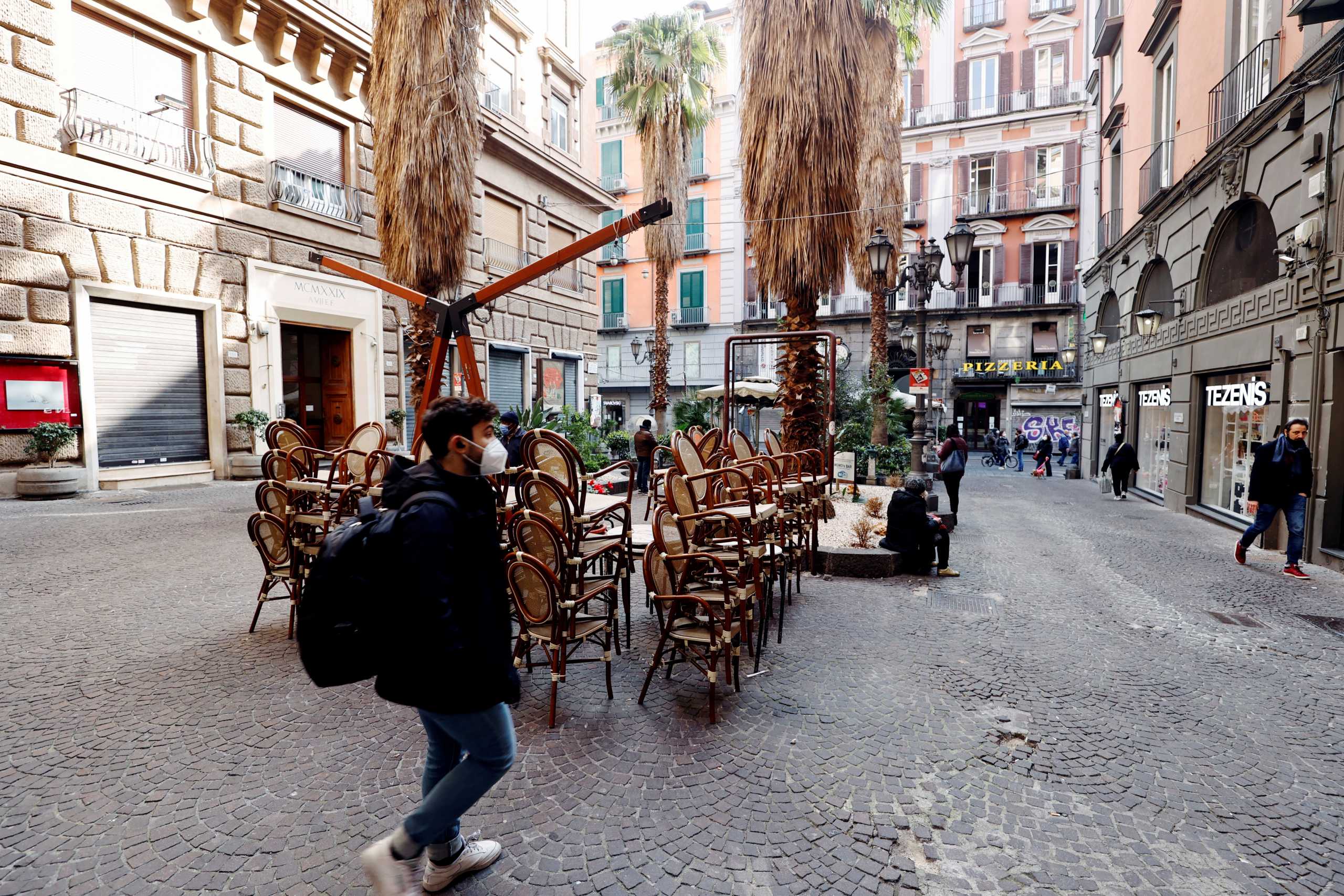 People walk past empty chairs after the region of Campania became a "red zone", increasing restrictions due to a rise in the coronavirus disease (COVID-19) infections, in Naples, Italy, March 8, 2021. REUTERS