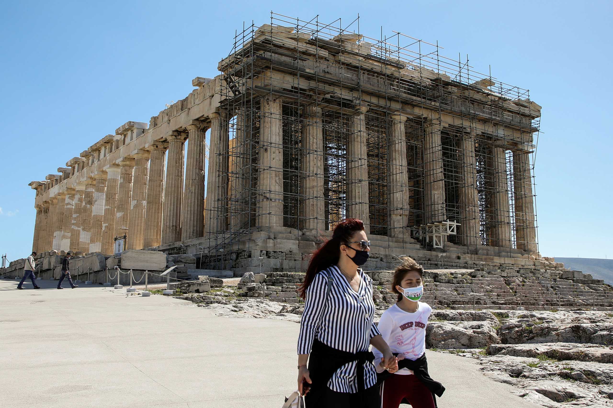 Visitors wearing protective face masks walk past the Parthenon temple atop the Acropolis hill, after archaeological sites open across Greece, following the easing of measures against the coronavirus disease (COVID-19), in Athens, Greece, March 22, 2021. REUTERS