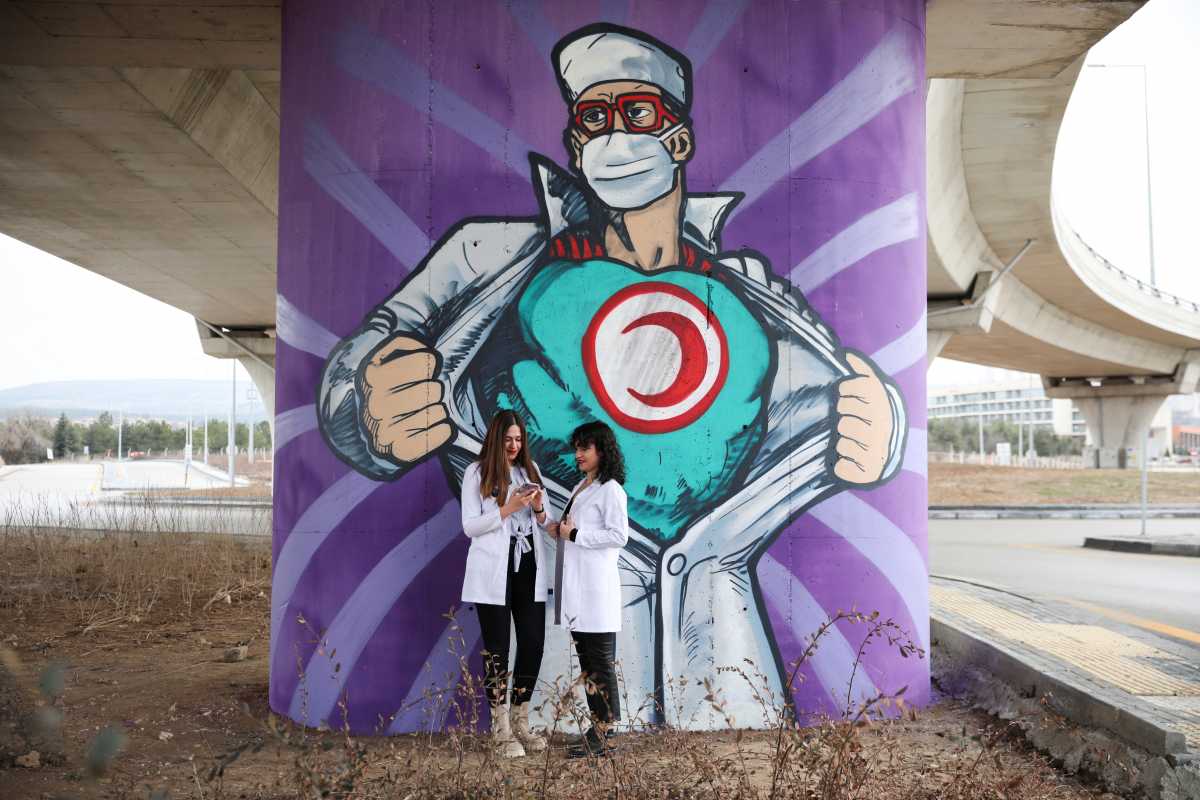 Medical students Busenur Zedef and her colleague stand in front of a graffiti, amid the coronavirus disease (COVID-19) outbreak, near the city hospital in Ankara, Turkey March 14, 2021. REUTERS