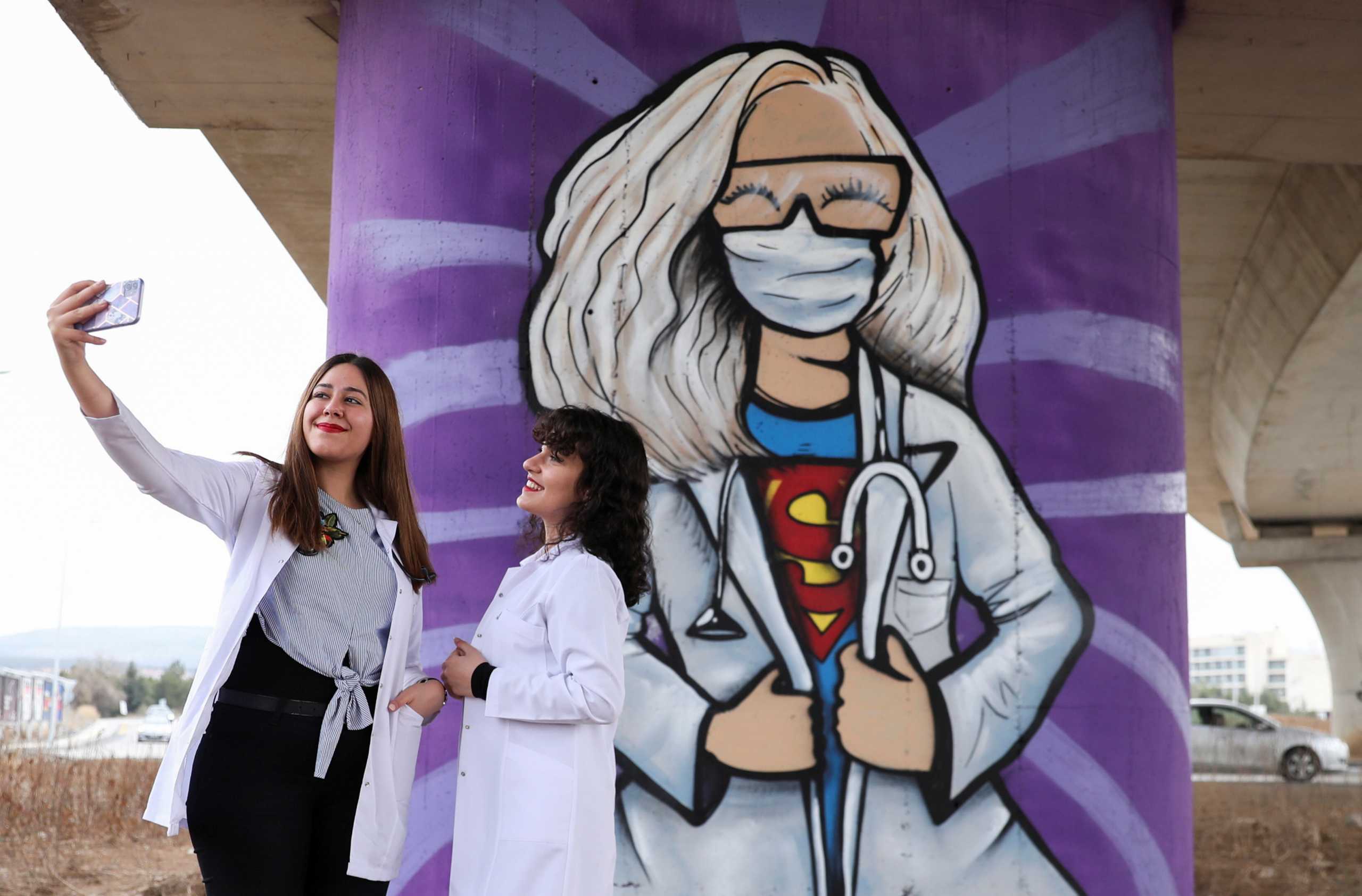 Medical students Busenur Zedef and her colleague pose for a selfie in front of a graffiti, amid the coronavirus disease (COVID-19) outbreak, near the city hospital in Ankara, Turkey March 14, 2021. REUTERS