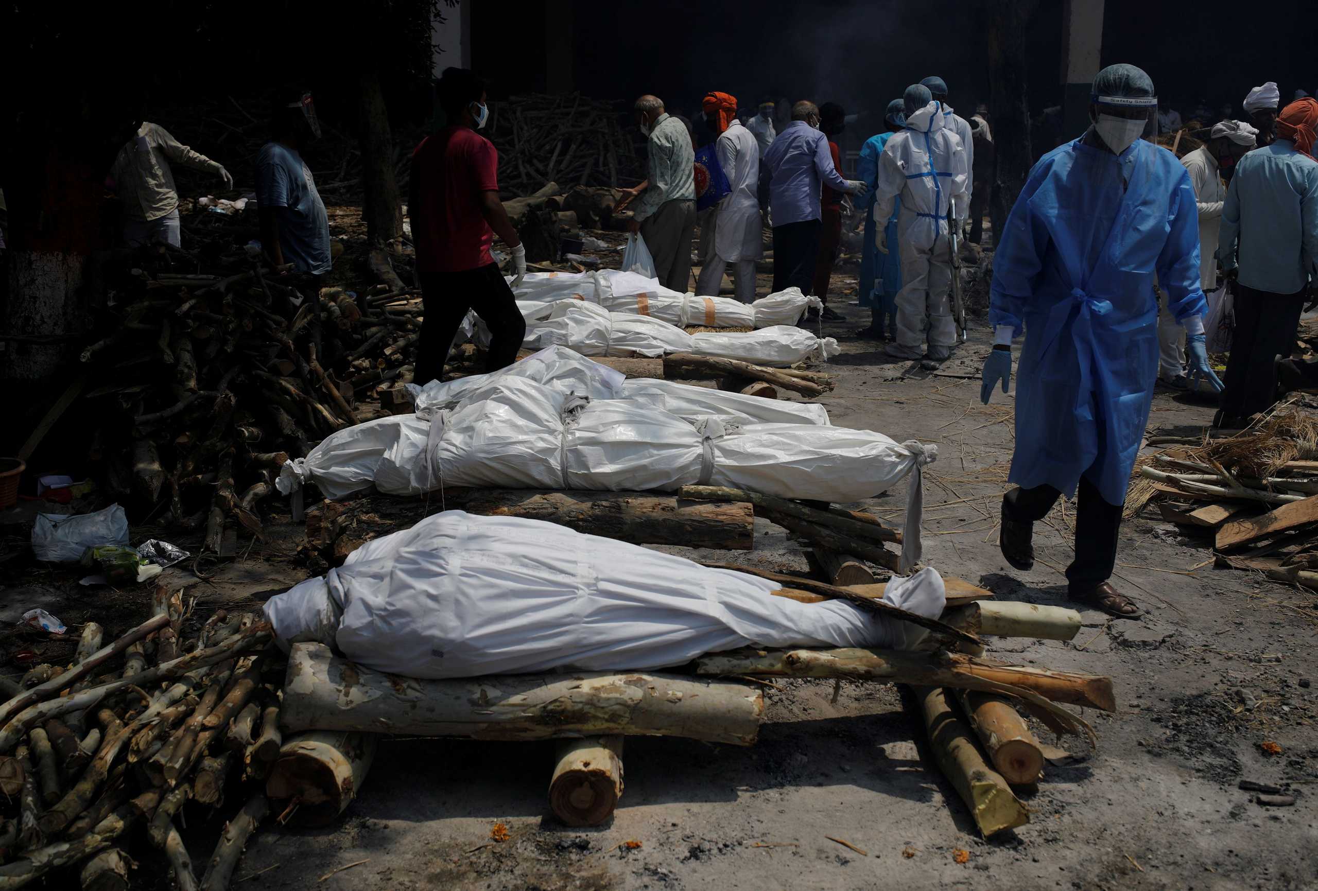 A health worker wearing personal protective equipment (PPE) walks past the funeral pyres of those who died from the coronavirus disease (COVID-19) during a mass cremation at a crematorium in New Delhi, India, April 26, 2021. REUTERS