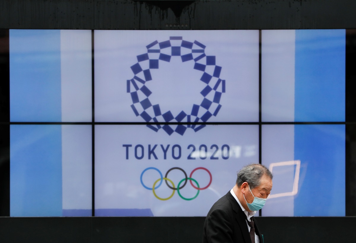 A passerby wearing a protective face mask walks past a screen showing the logo of the Tokyo 2020 Olympic Games that have been postponed to 2021 due to the coronavirus disease (COVID-19) pandemic, in Tokyo, Japan, April 14, 2021.   REUTERS