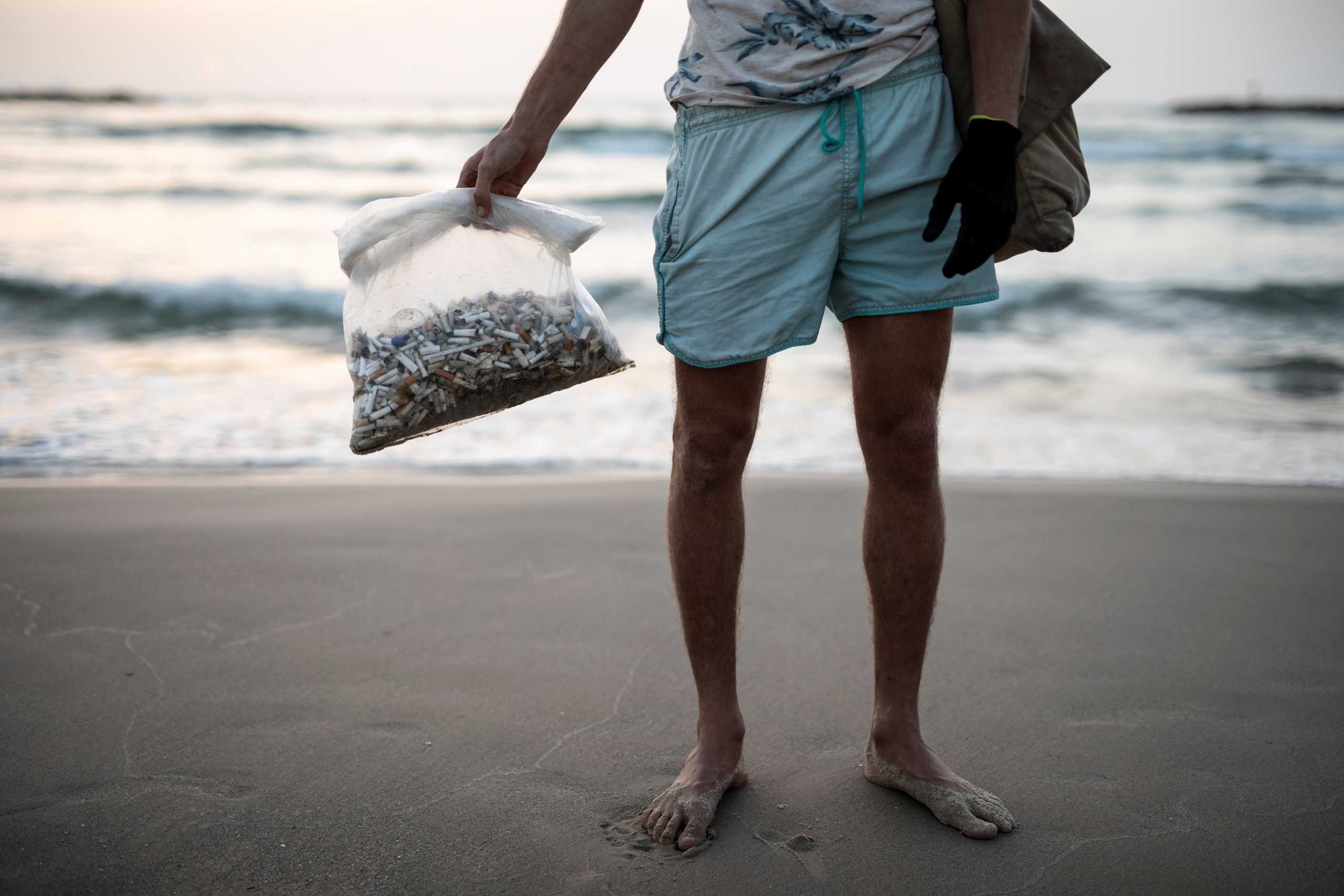 Julian Melcer holds a plastic bag filled with cigarette butts he collected from the shore of the Mediterranean Sea as part of environmental campaign, at a beach, in Tel Aviv, Israel April 20, 2021. Picture taken April 20, 2021. REUTERS
