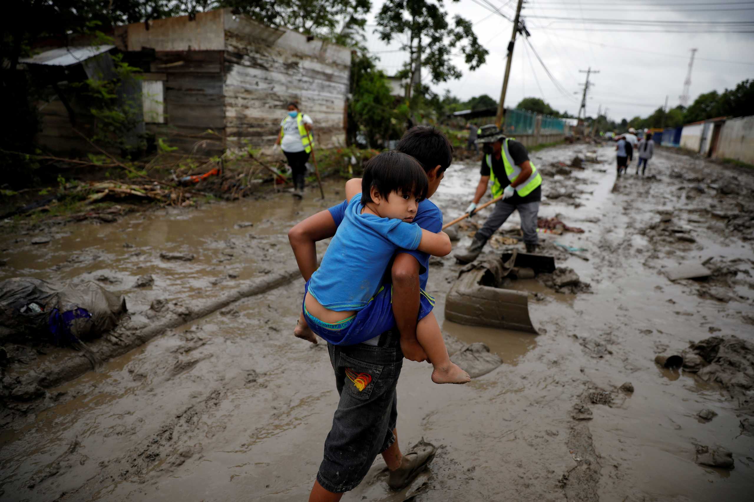 FILE PHOTO: A child carries his brother in a street covered in mud after the floods caused by the rains brought by Hurricanes Eta and Iota, in La Lima, Honduras December 8, 2020. Picture taken December 8, 2020. REUTERS