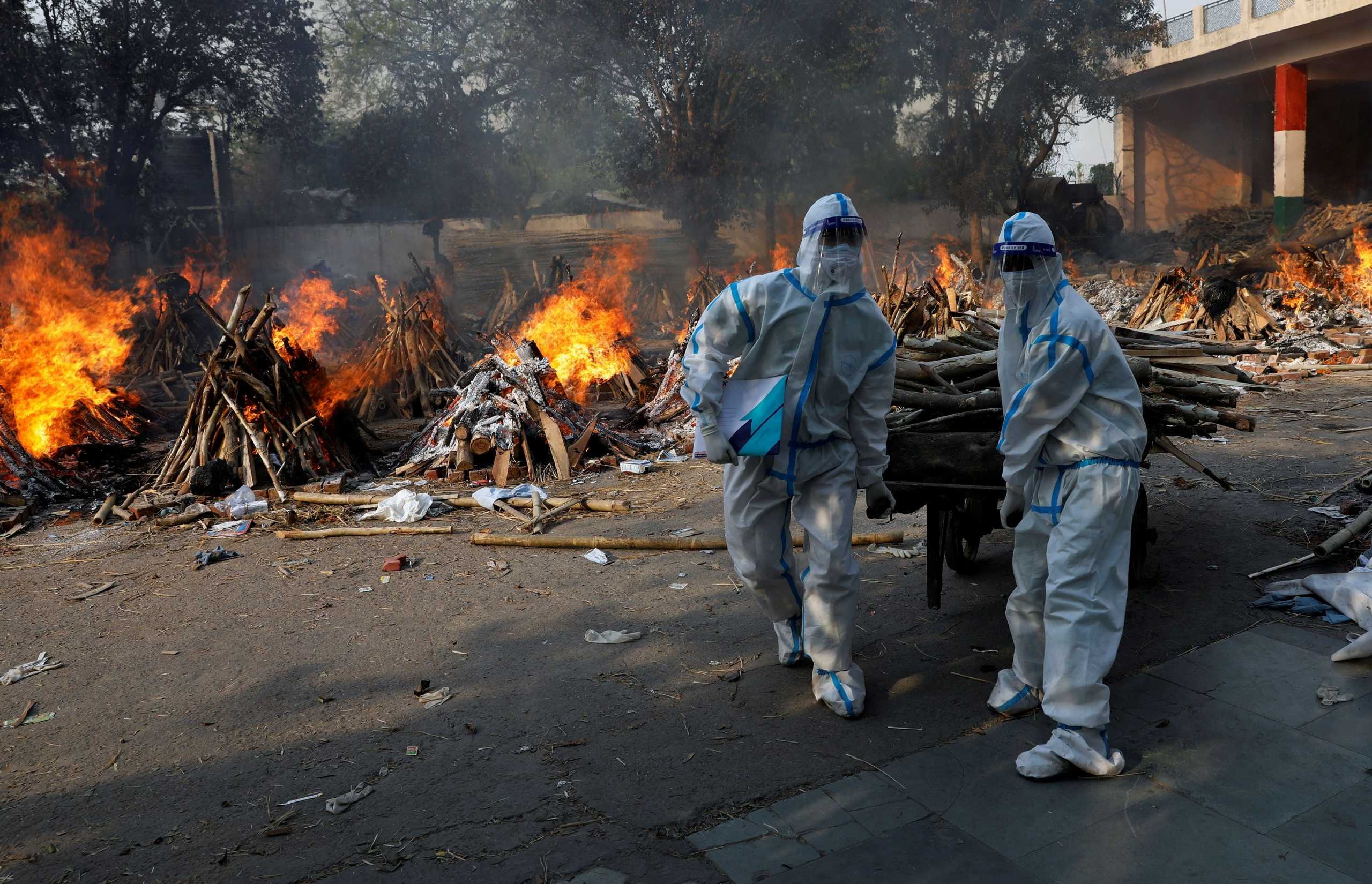 Health workers wearing personal protective equipment (PPE) carry wood to prepare a funeral pyre for a coronavirus disease (COVID-19) victim during a mass cremation at a crematorium in New Delhi, India, April 26, 2021. REUTERS