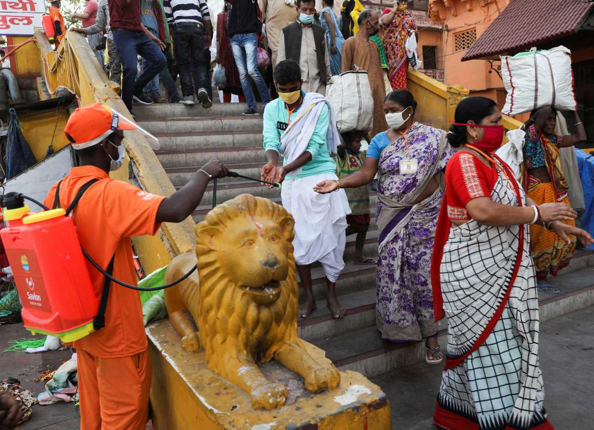 A frontline worker sprays disinfectant on the hands of devotees, on the banks of the Ganges river during Kumbh Mela, or the Pitcher Festival, amidst the spread of the coronavirus disease (COVID-19), in Haridwar, India, April 12, 2021. REUTERS