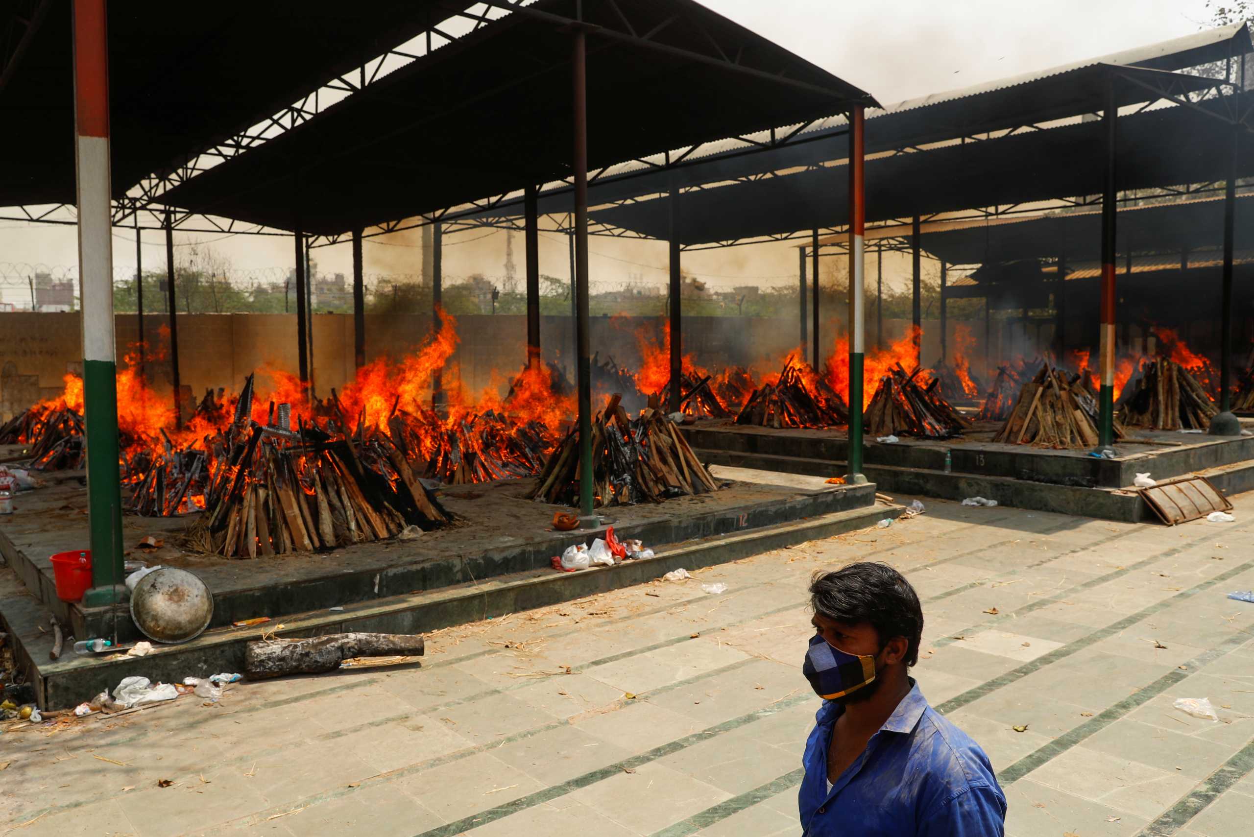 A man walks past the burning funeral pyres of those who died from the coronavirus disease (COVID-19), during a mass cremation, at a crematorium in New Delhi, India April 26, 2021. REUTERS