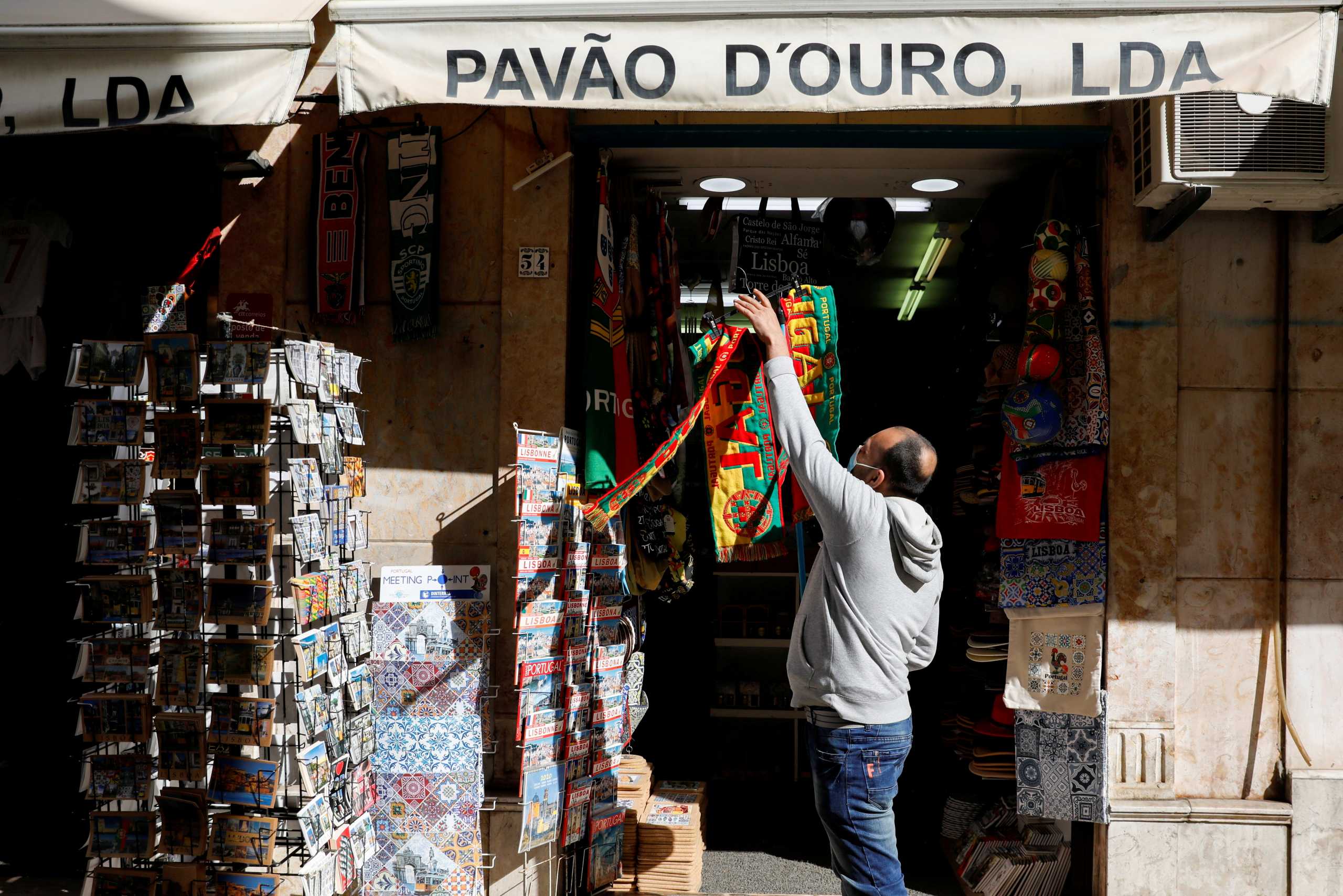 FILE PHOTO: A man hangs football scarves in a store on the first day of the reopening after a country lockdown, amid the coronavirus disease (COVID-19) pandemic, in Lisbon, Portugal, April 5, 2021. REUTERS