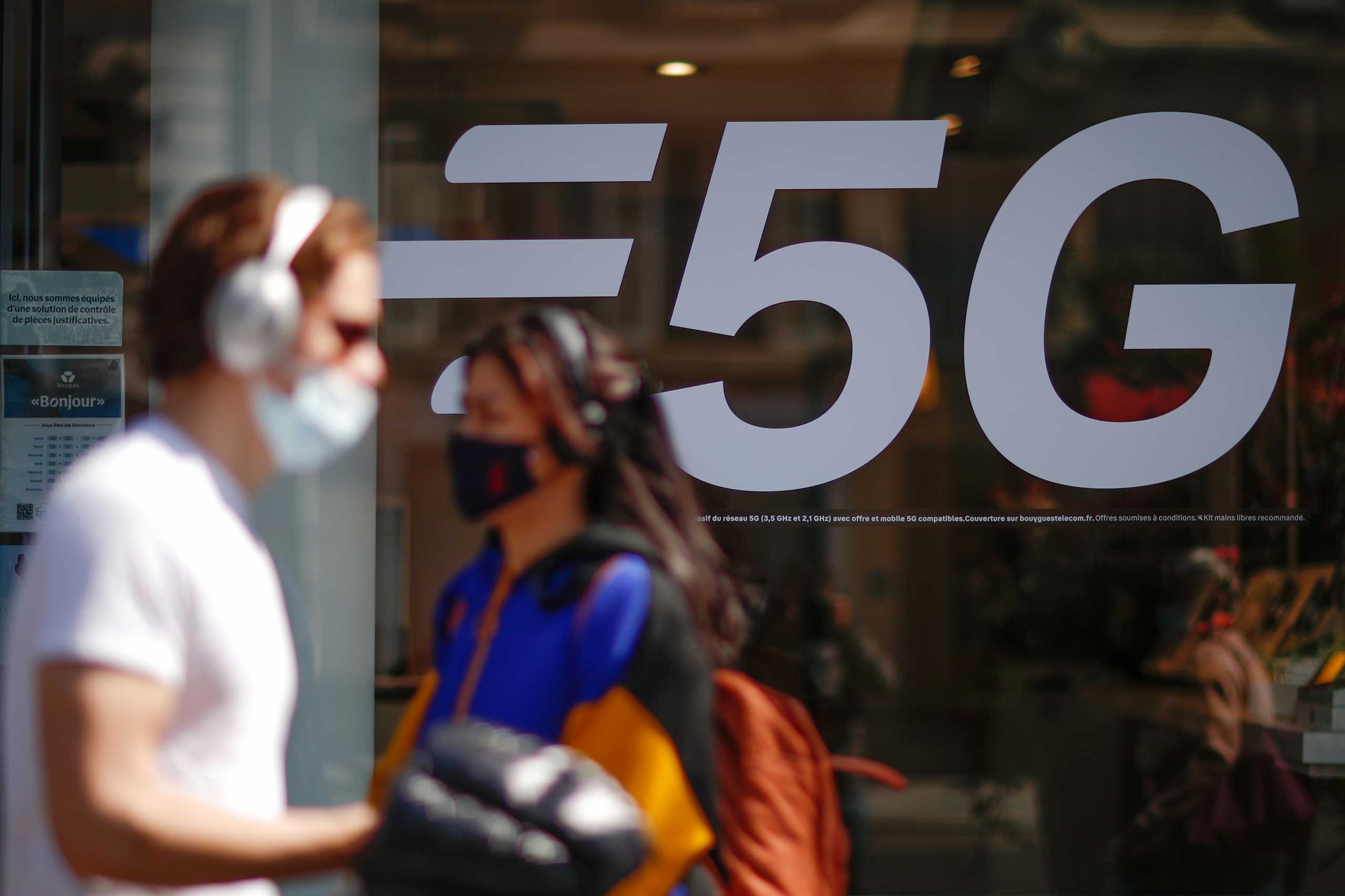 People, wearing protective face masks, walk past a 5G data network sign at a mobile phone store in Paris, France, April 22, 2021. REUTERS