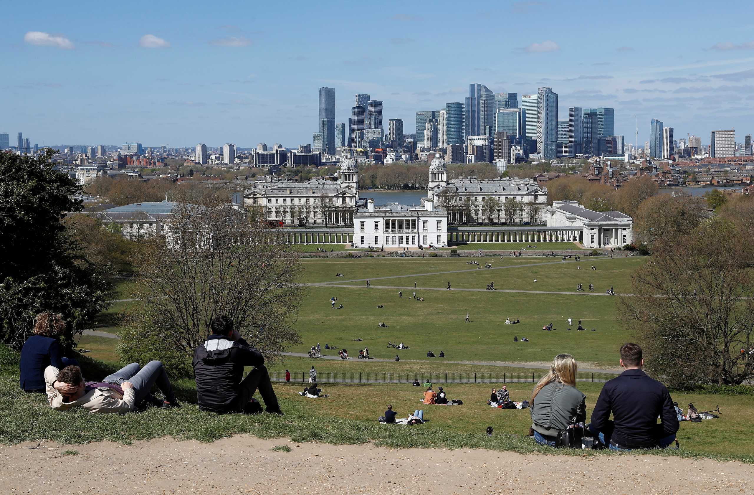 Visitors to Greenwich Park sit and look towards Canary Wharf financial district as lockdown restrictions are eased amidst the spread of the coronavirus disease (COVID-19) pandemic in London, Britain, April 25, 2021. REUTERS