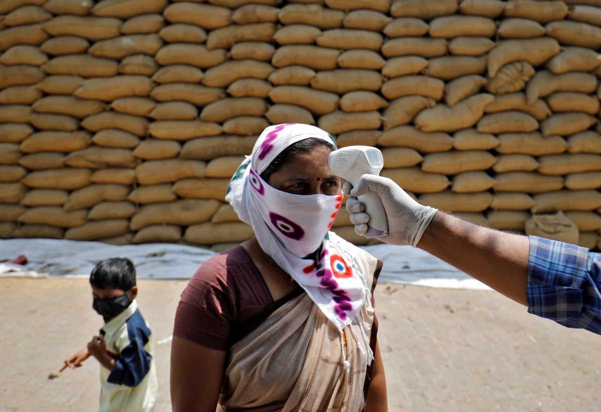 FILE PHOTO: A healthcare worker checks the temperature of a rice mill worker during a coronavirus disease (COVID-19) vaccination drive at Bavla village on the outskirts of Ahmedabad, India, April 13, 2021. REUTERS
