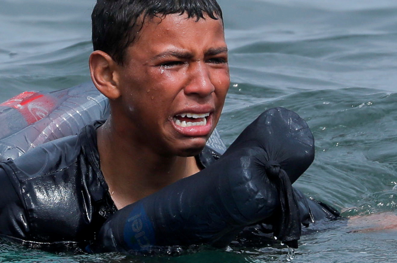 A Moroccan boy cries as he swims using bottles as a float, near the fence between the Spanish-Moroccan border, after thousands of migrants swam across the border, in Ceuta, Spain, May 19, 2021. Picture taken May 19, 2021. REUTERS