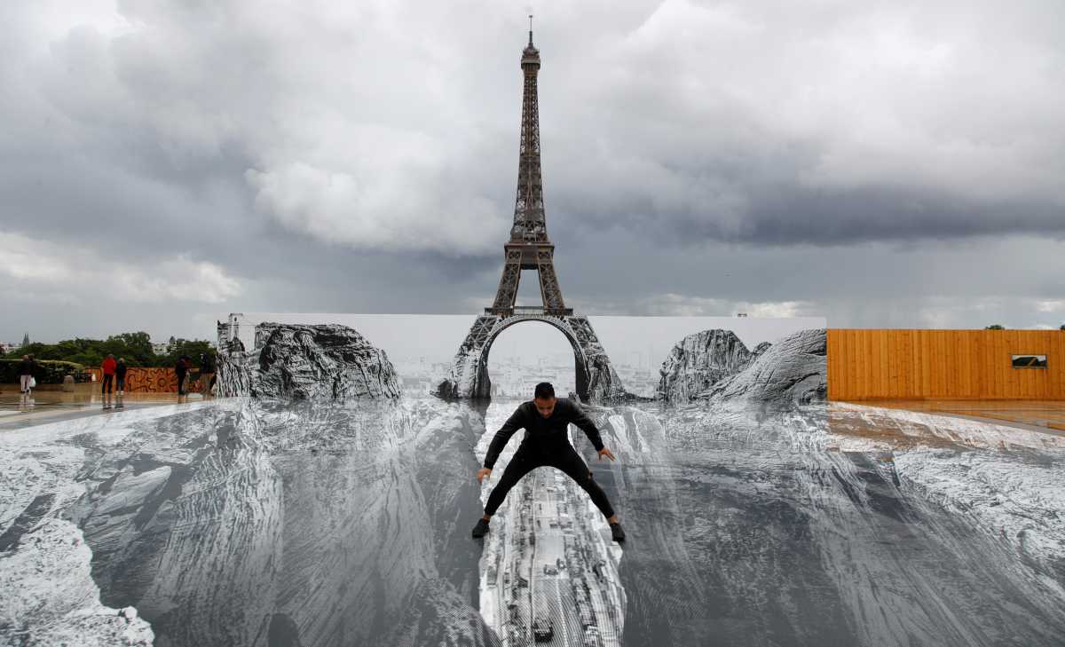 A man poses on a giant artwork by French artist JR installed on the Trocadero square in front of the Eiffel Tower in Paris, France, May 19, 2021. REUTERS