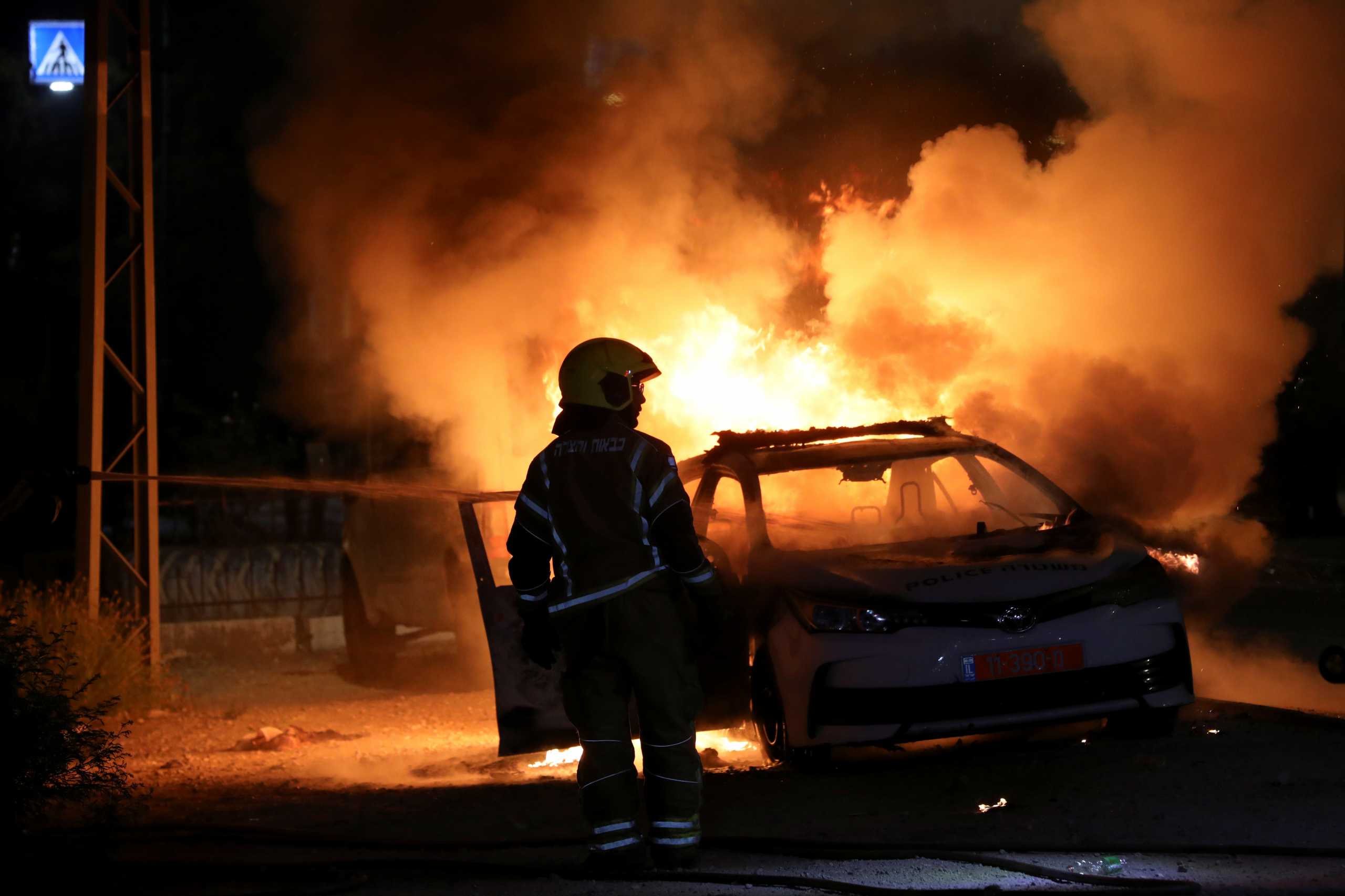 An Israeli firefighter stands near a burning Israeli police car during clashes between Israeli police and members of the country's Arab minority in the Arab-Jewish town of Lod, Israel May 12, 2021. REUTERS