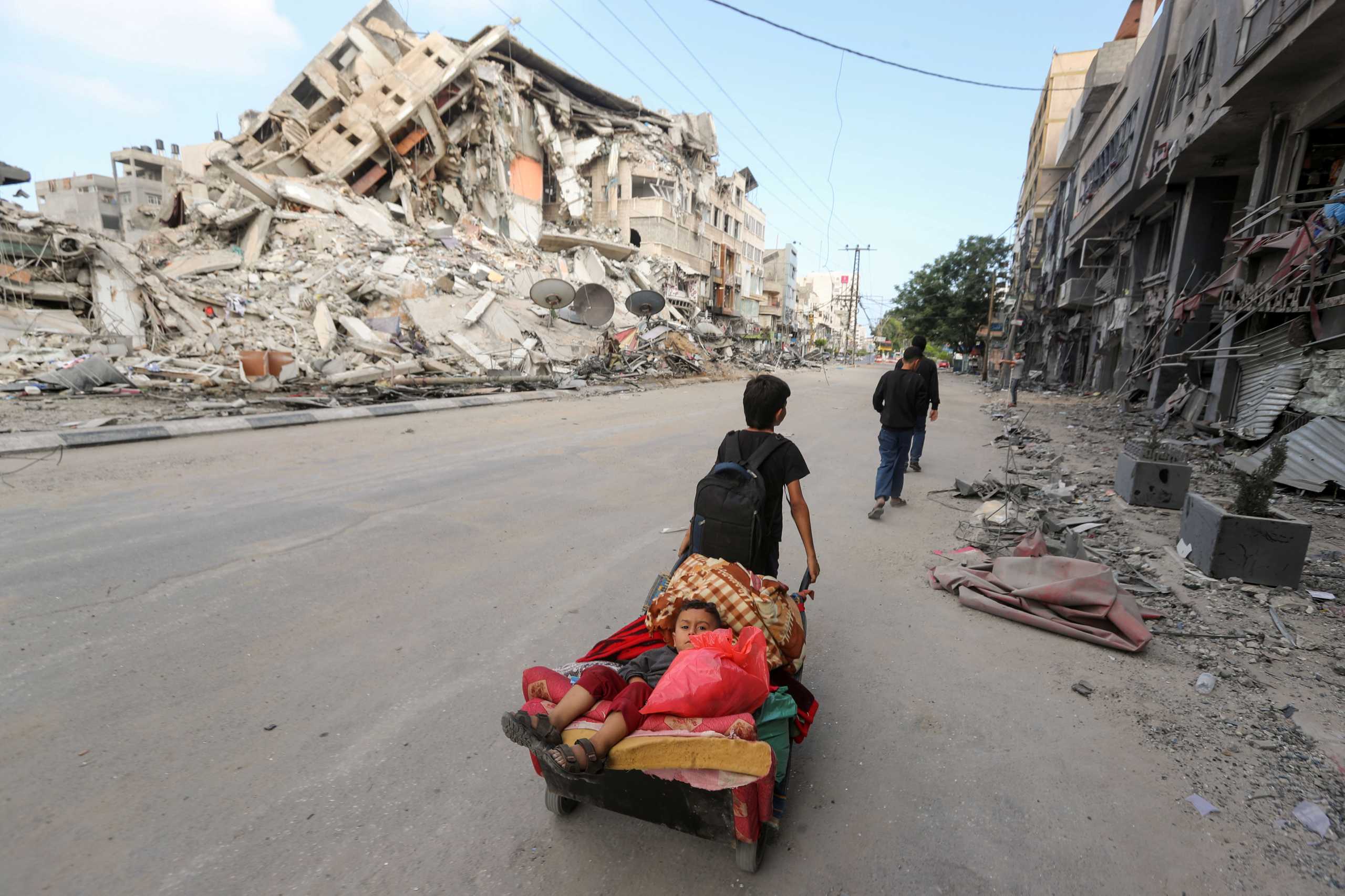 A Palestinian boy pulls a cart carrying his brother and their belongings as they flee their home during Israeli air and artillery strikes, near the site of a tower building destroyed in earlier strikes in Gaza City May 14, 2021. REUTERS