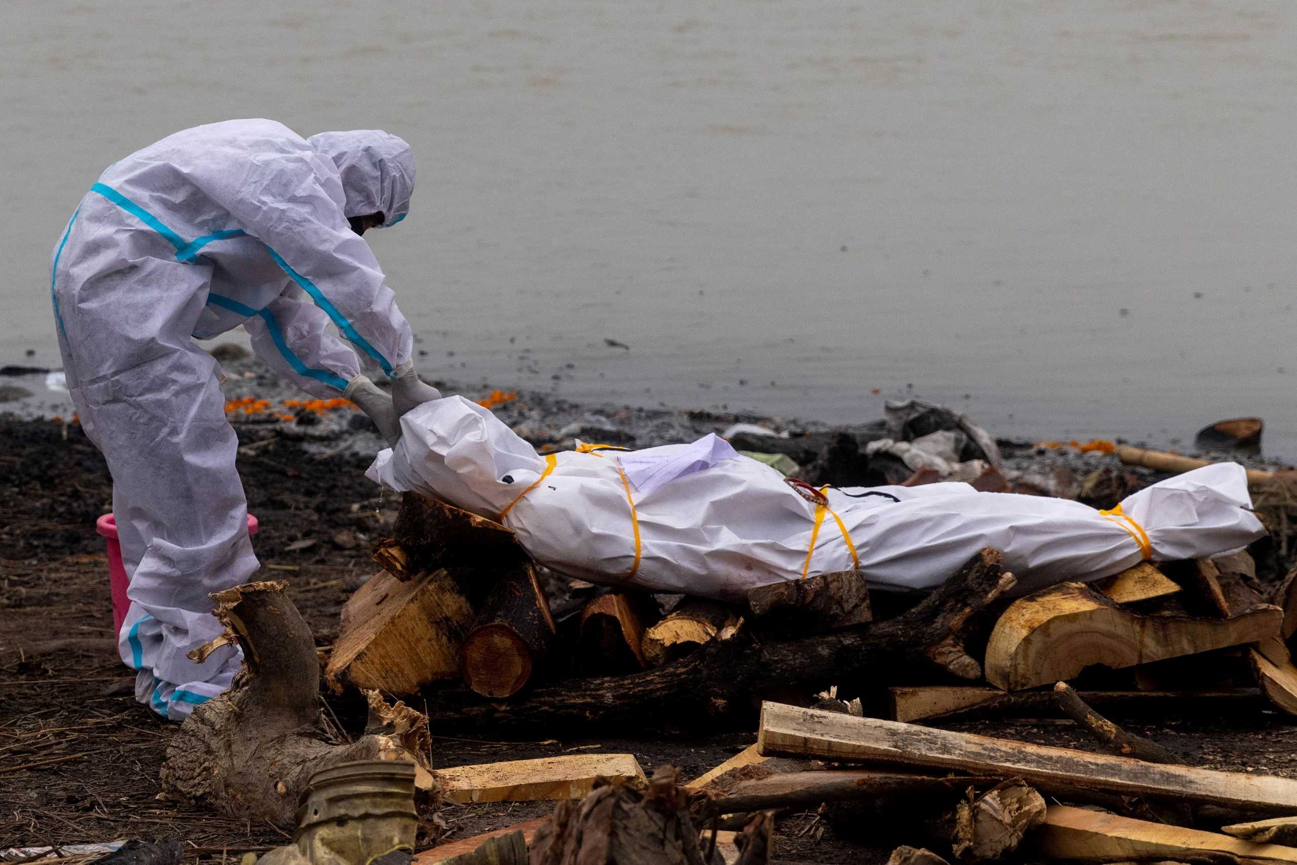 FILE PHOTO: A man wearing a protective suit touches the body of his relative, who died from the coronavirus disease (COVID-19), before his cremation on the banks of the river Ganges at Garhmukteshwar in the northern state of Uttar Pradesh, India, May 6, 2021. REUTERS