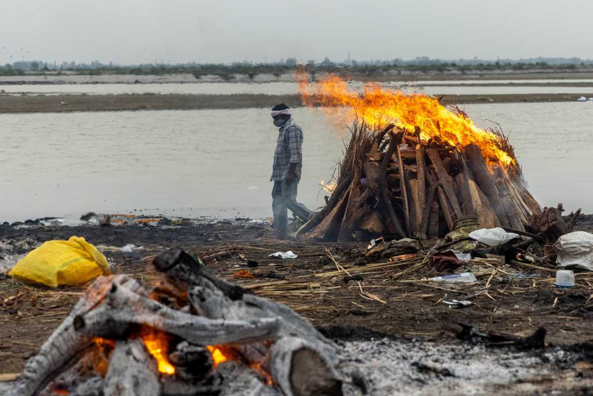A man walks past burning pyres with people who died from the coronavirus disease (COVID-19), on the banks of the river Ganges at Garhmukteshwar in the northern state of Uttar Pradesh, India, May 6, 2021. REUTERS