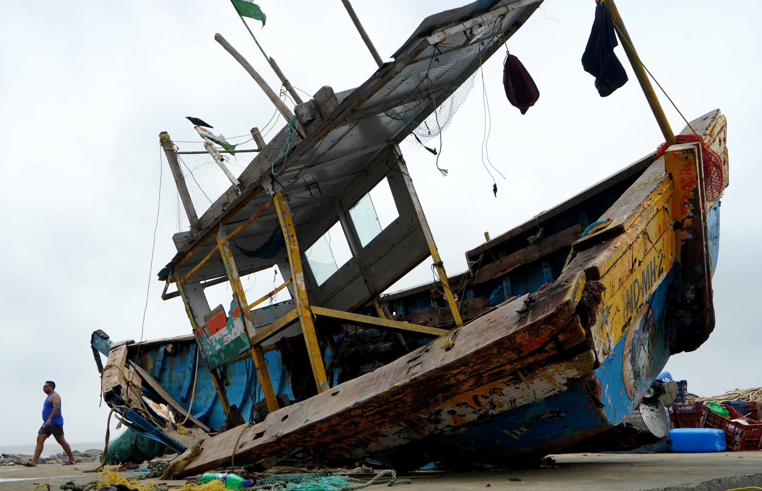 A man walks past a damaged fishing boat on a shore after heavy winds caused by Cyclone Tauktae, in Mumbai, India, May 18, 2021. REUTERS