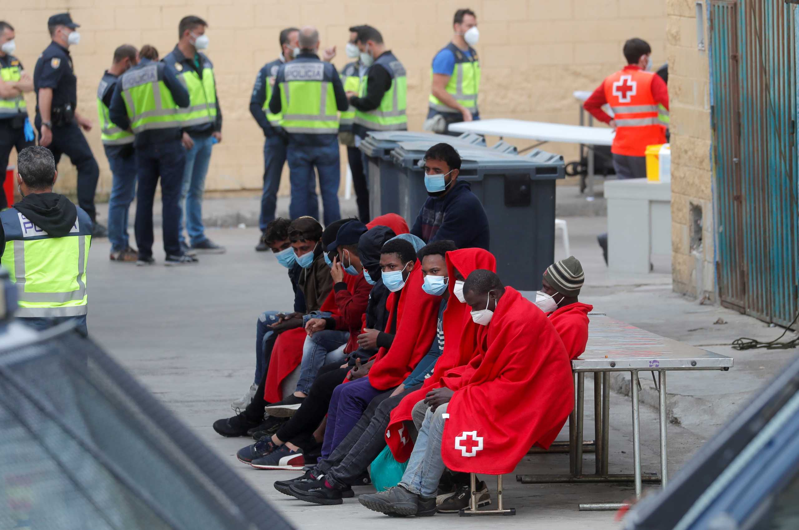 Migrants sit outside a facility prepared for them, accompanied by members of a NGO and Spanish police officers, near the Spanish-Moroccan border, after thousands of migrants swam across this border during the last days, in Ceuta, Spain, May 21, 2021. REUTERS