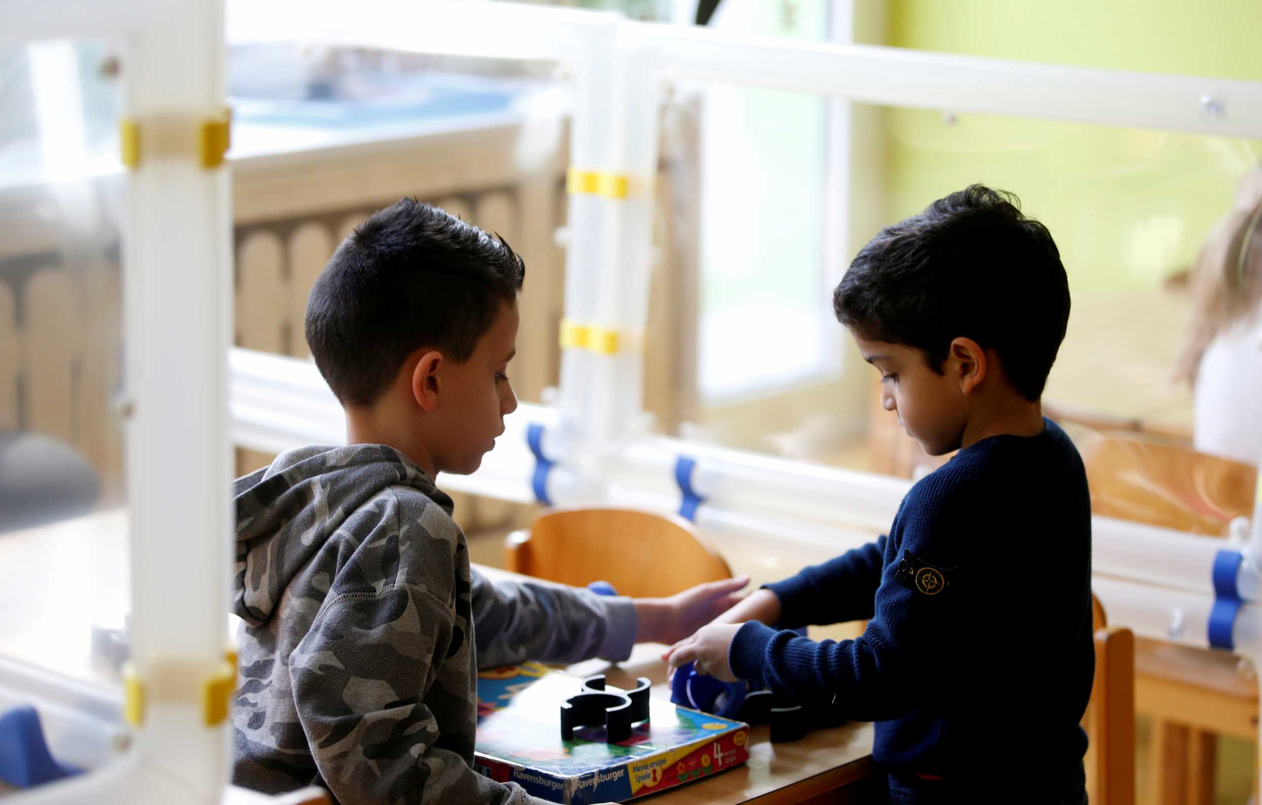 FILE PHOTO: Children play at their tables during a demonstration of the use of sneeze guards at a nursery school as the spread of the coronavirus disease (COVID-19) continues, Velbert, Germany, April 8, 2021. Picture taken April 8, 2021. REUTERS