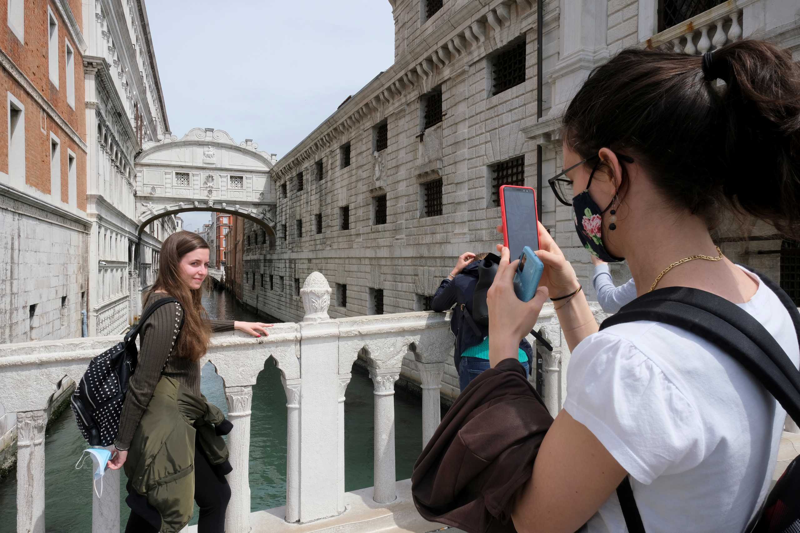 Tourists take pictures on a bridge as Italy lifts quarantine restrictions for travellers arriving from European Union countries, Britain and Israel and begins offering COVID-free flights in a bid to revive the tourism industry, in Venice, Italy, May 16, 2021. REUTERS
