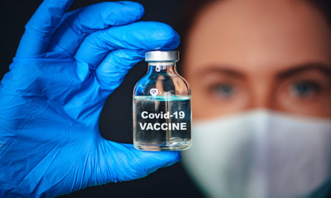 Coronavirus Covid-19 Protection and Vaccination. Closeup of portrait, doctor with a bottle of vaccine. Tittle on bottle "Covid-19 VACCINE"