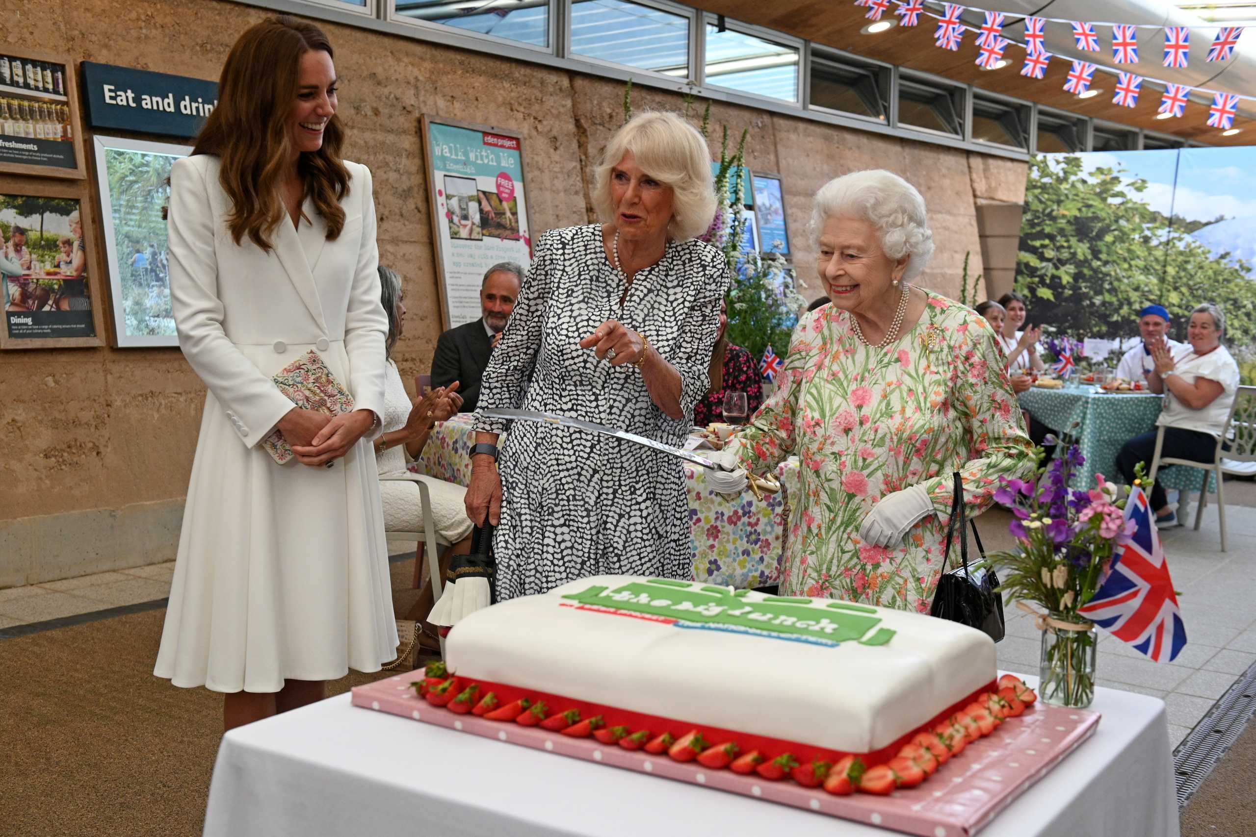 Britain's Queen Elizabeth holds a sword in order to cut a cake next to Catherine, the Duchess of Cambridge and Camilla,  Duchess of Cornwall during a drinks reception on the sidelines of the G7 summit, at the Eden Project in Cornwall, Britain June 11, 2021. Oli Scarff