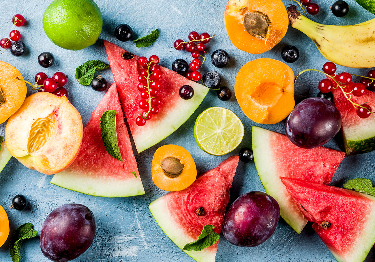Summer vitamin food concept, various fruit and berries watermelon peach mint plum apricots blueberry currant, creative flat lay on light blue background top view copy space banner
