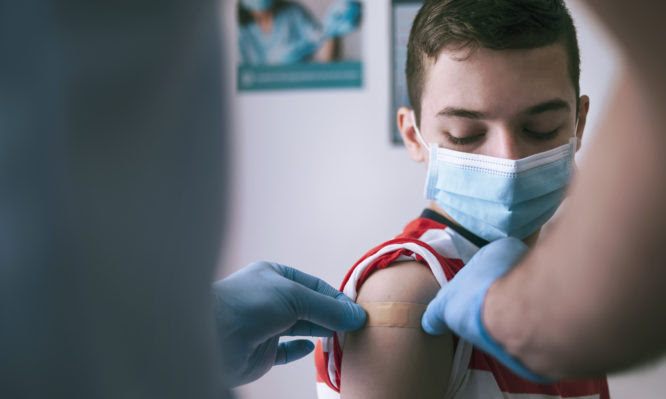 Doctor putting adhesive bandage to a teenage boy after Covid-19 vaccine injection.